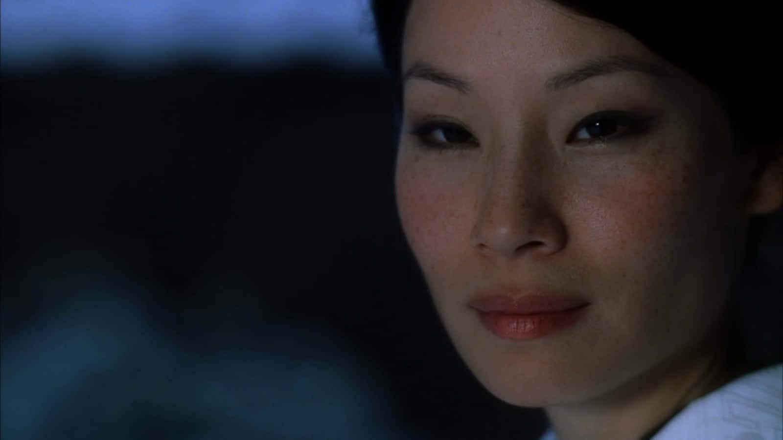 lucy liu 桌布 壁紙 — 一個女人的臉部特寫，在昏暗的藍色調中柔和地照亮，背景是模糊的黑暗。