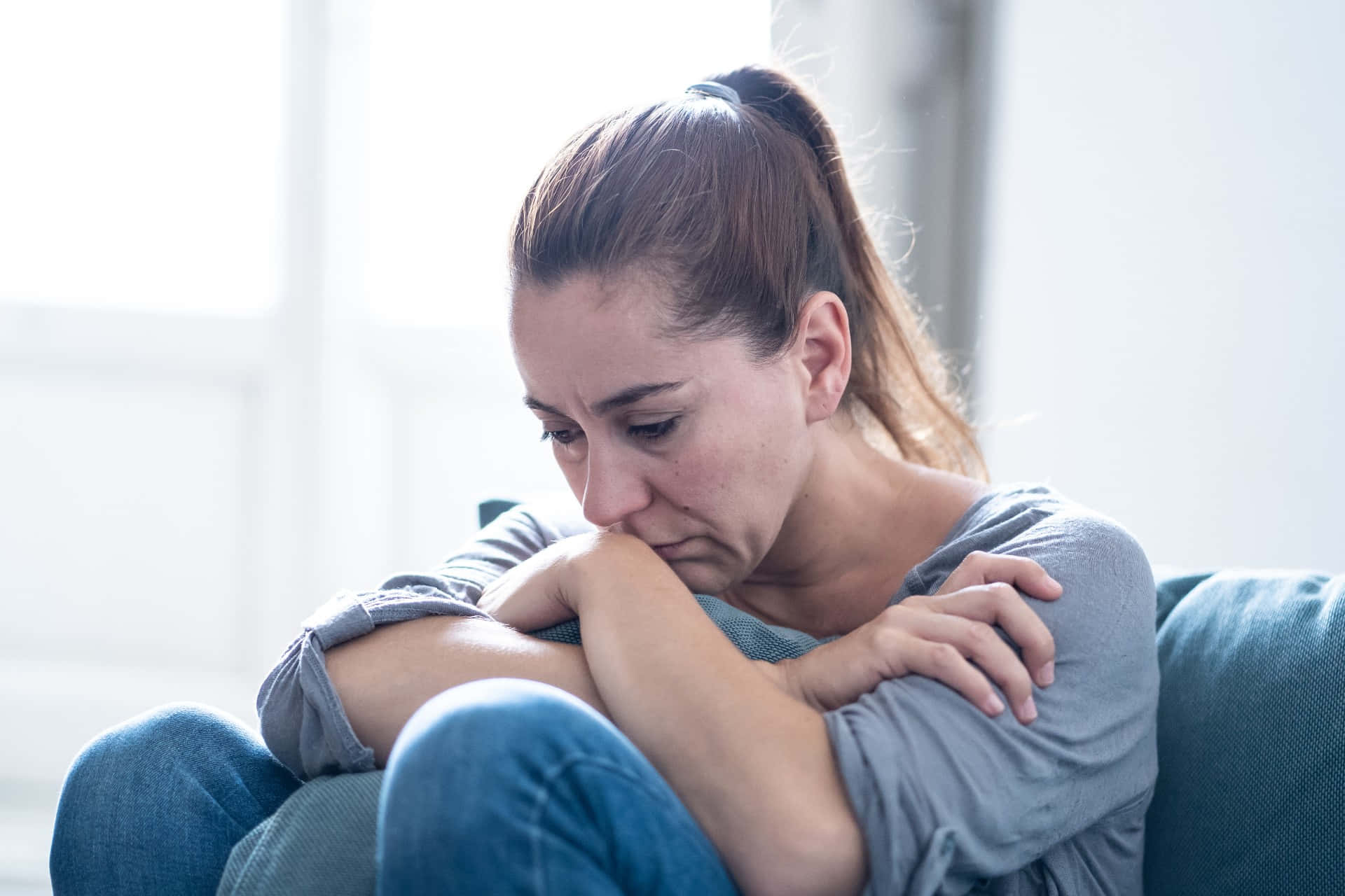Depressed 桌布 壁紙 — 一個女人蜷縮在沙發上，頭靠在手臂上，神情沮喪，房間光線柔和。
