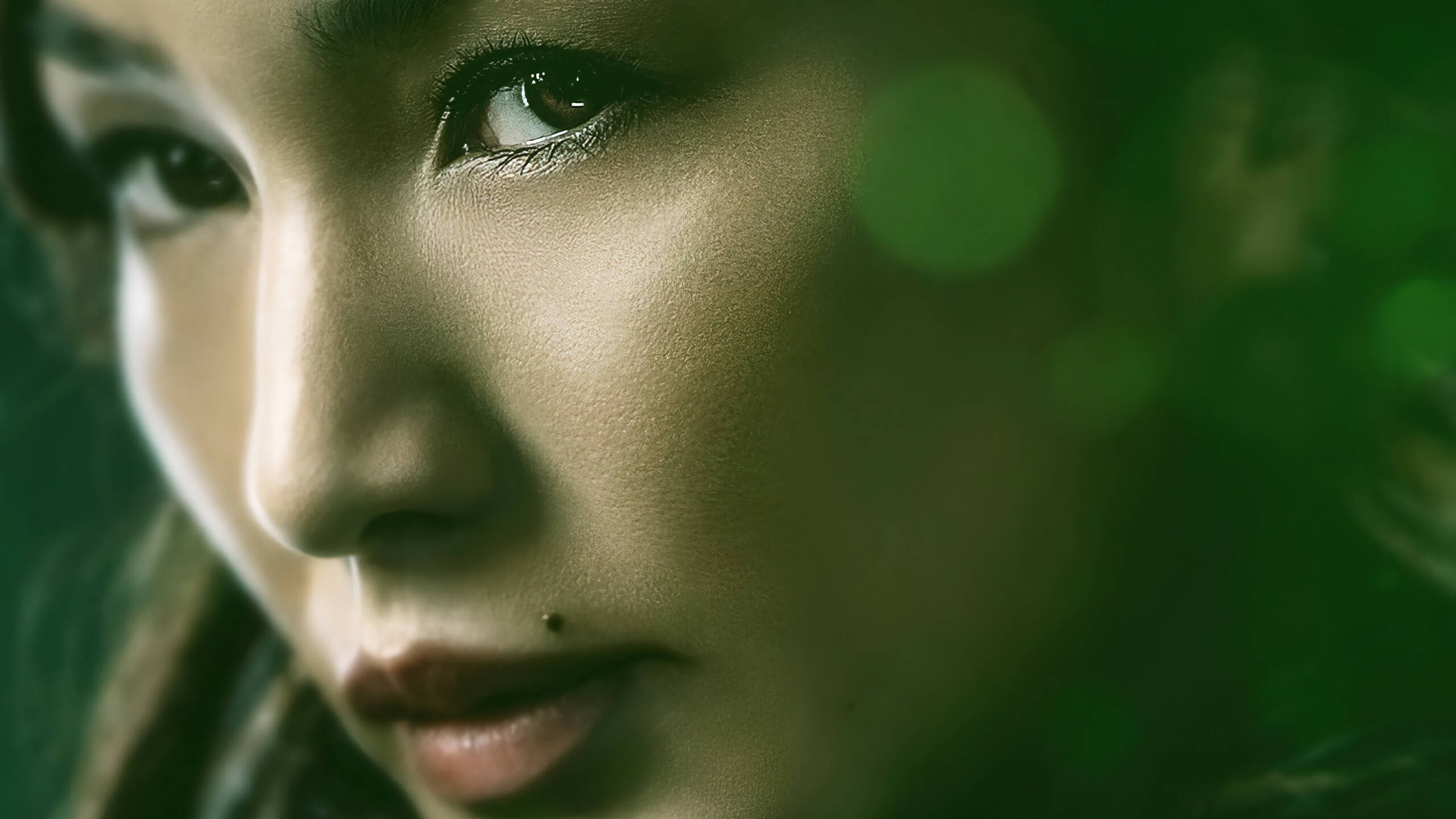 Eternals 桌布 壁紙 — 一個女性臉部的特寫肖像，帶有柔和的綠色散景和溫暖的燈光，凸顯她沉思的目光。