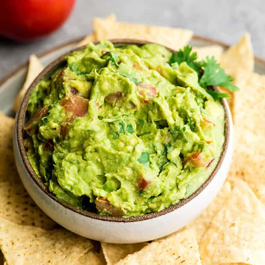 Mexican 桌布 壁紙 — 一個奶油狀的綠色酪梨醬，上面放著香菜和洋蔥，放在一個陶瓷碗裡，周圍是玉米片。