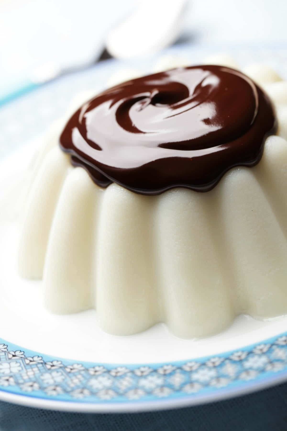 Blancmange 桌布 壁紙 — 一個奶油白色法式燉蛋，帶有光澤的深色巧克力漩渦，放在藍色花卉盤上。