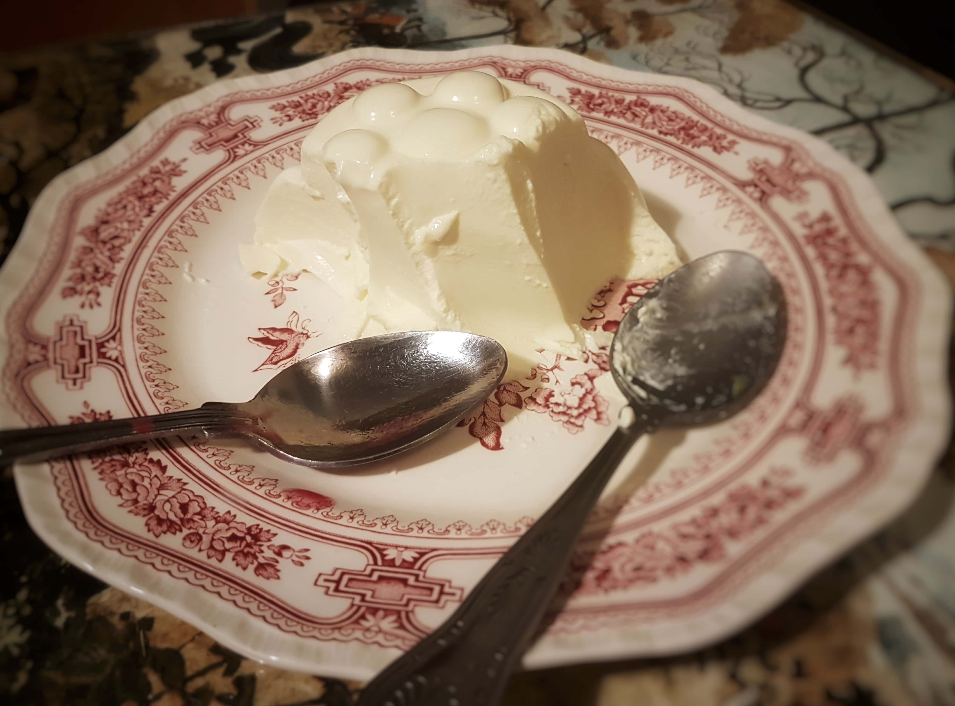 Blancmange 桌布 壁紙 — 一個奶油白色的慕斯優雅地放在復古紅色花卉盤上，旁邊有兩隻湯匙。
