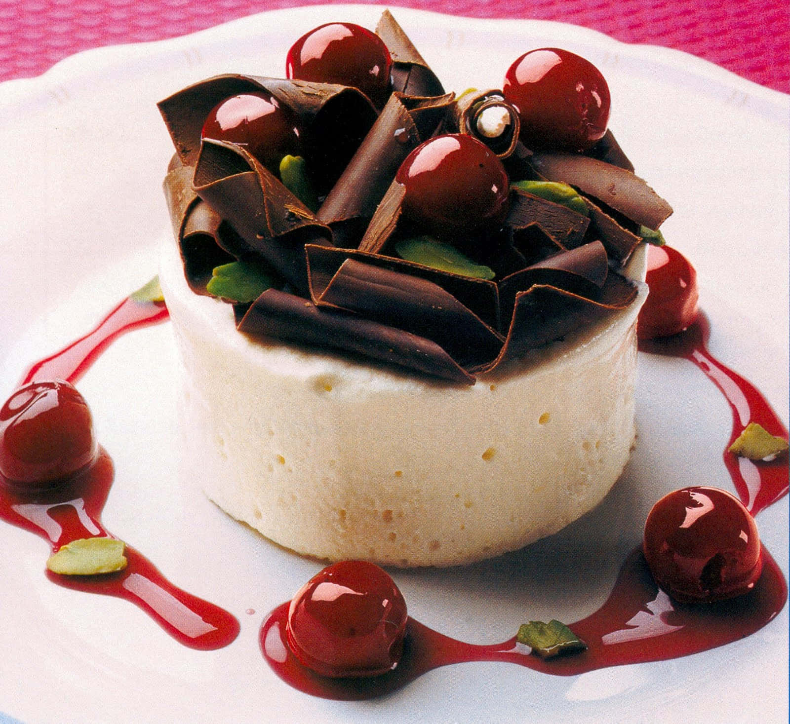甜點 桌布 壁紙 — 一個奶油白色的甜點，上面放有光澤的櫻桃和黑巧克力卷，放在白色盤子上，搭配紅色醬汁。