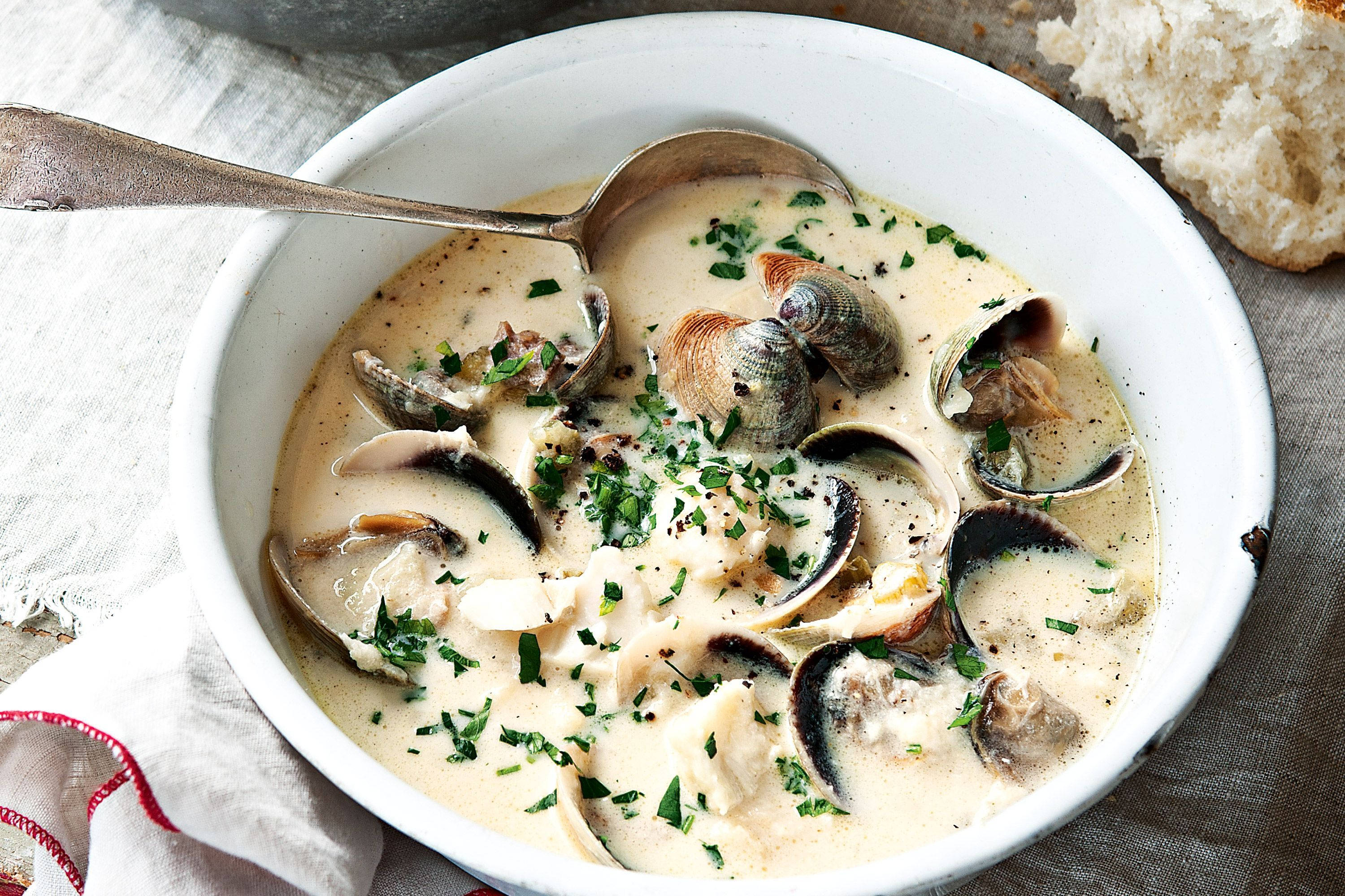 Chowder 桌布 壁紙 — 一個奶油白色的碗，裡面裝著蜆肉湯，飾以新鮮歐芹和黑胡椒，旁邊有一個鄉村風格的麵包卷。