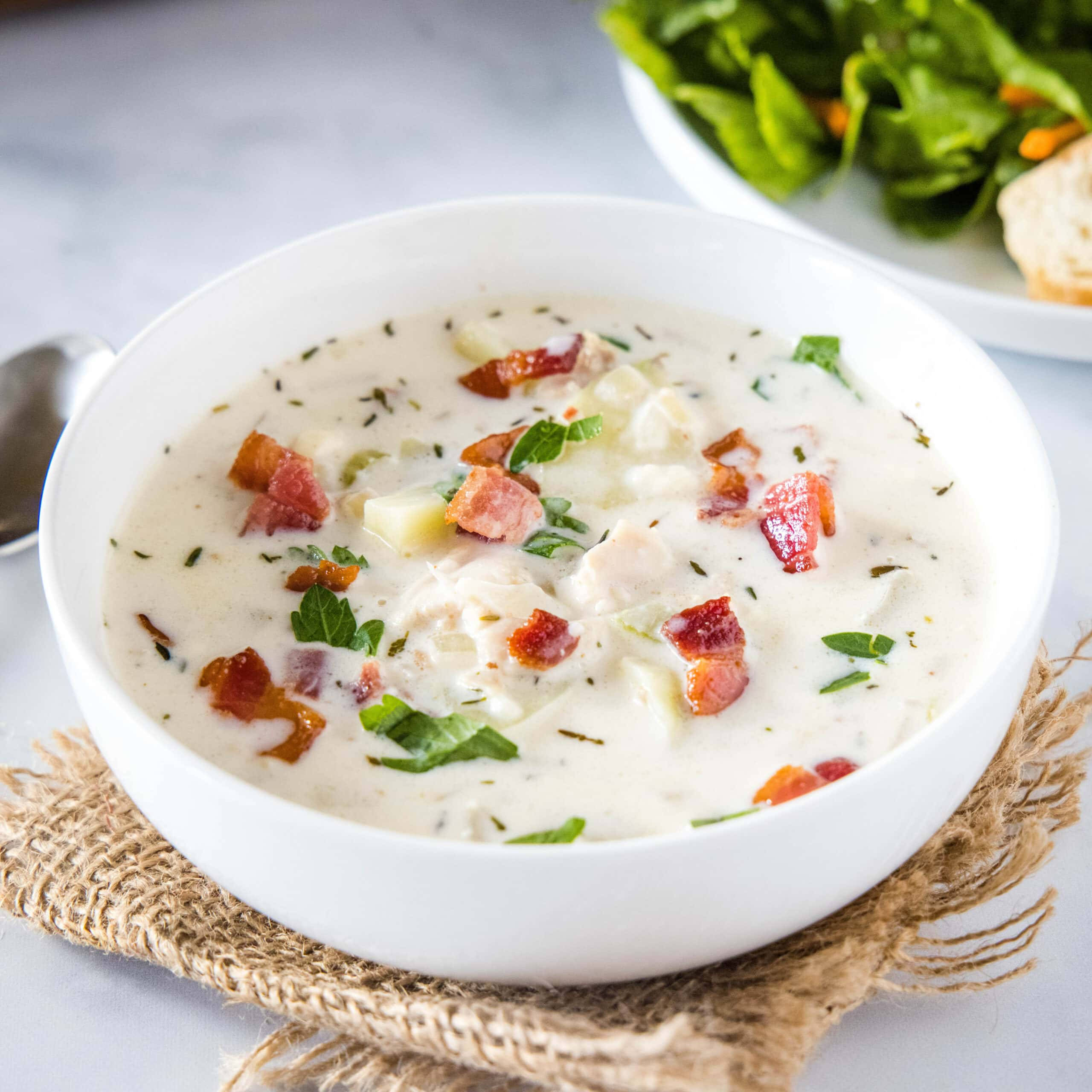 Soup 桌布 壁紙 — 一個奶油白色的蛤蜊濃湯碗，上面放著酥脆的培根和新鮮的歐芹，放在質樸的黃麻墊上。