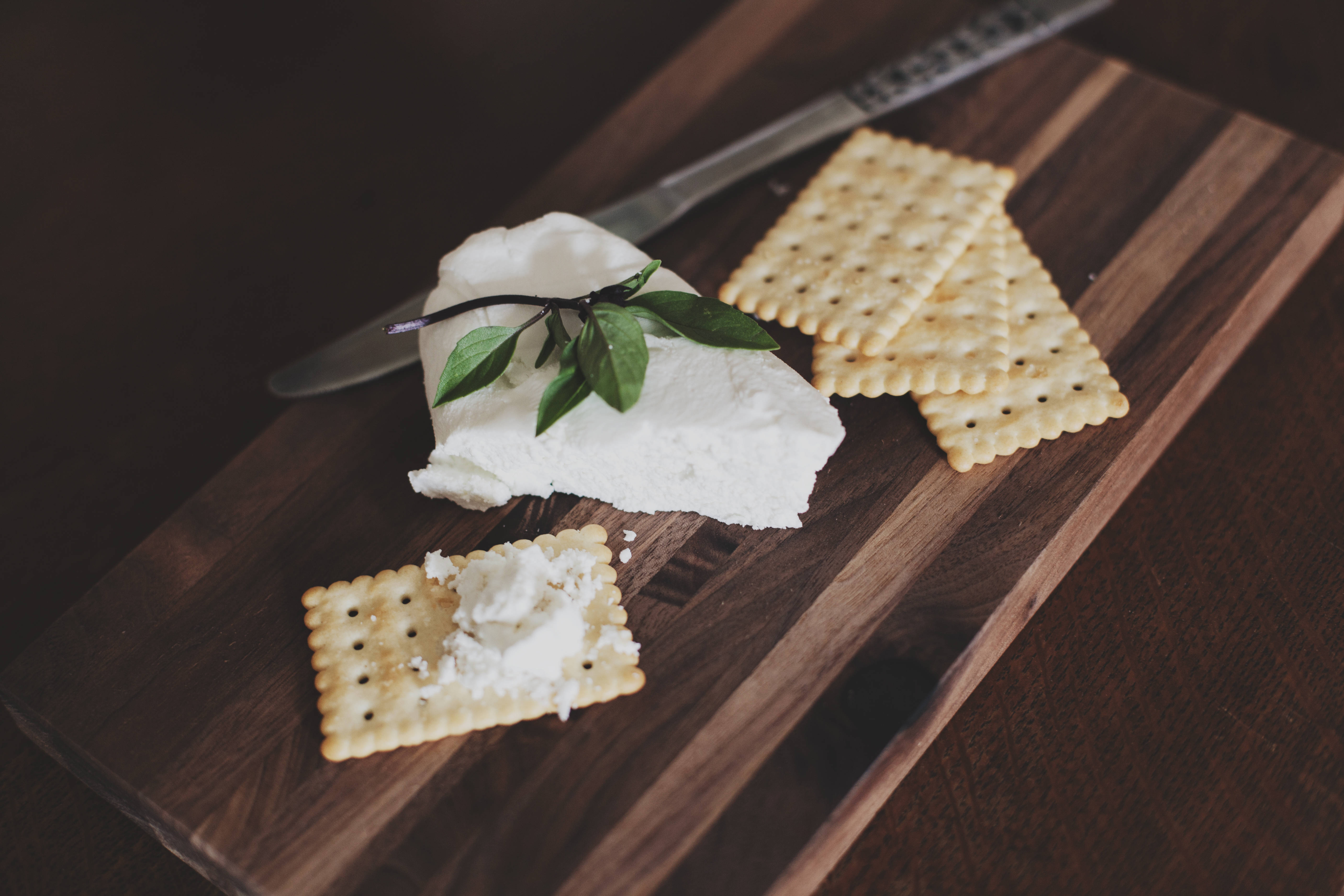 crackers 桌布 壁紙 — 一個奶油白色的起司，飾以新鮮綠葉，旁邊放著鹹餅乾，在深色木板上配有一把刀。