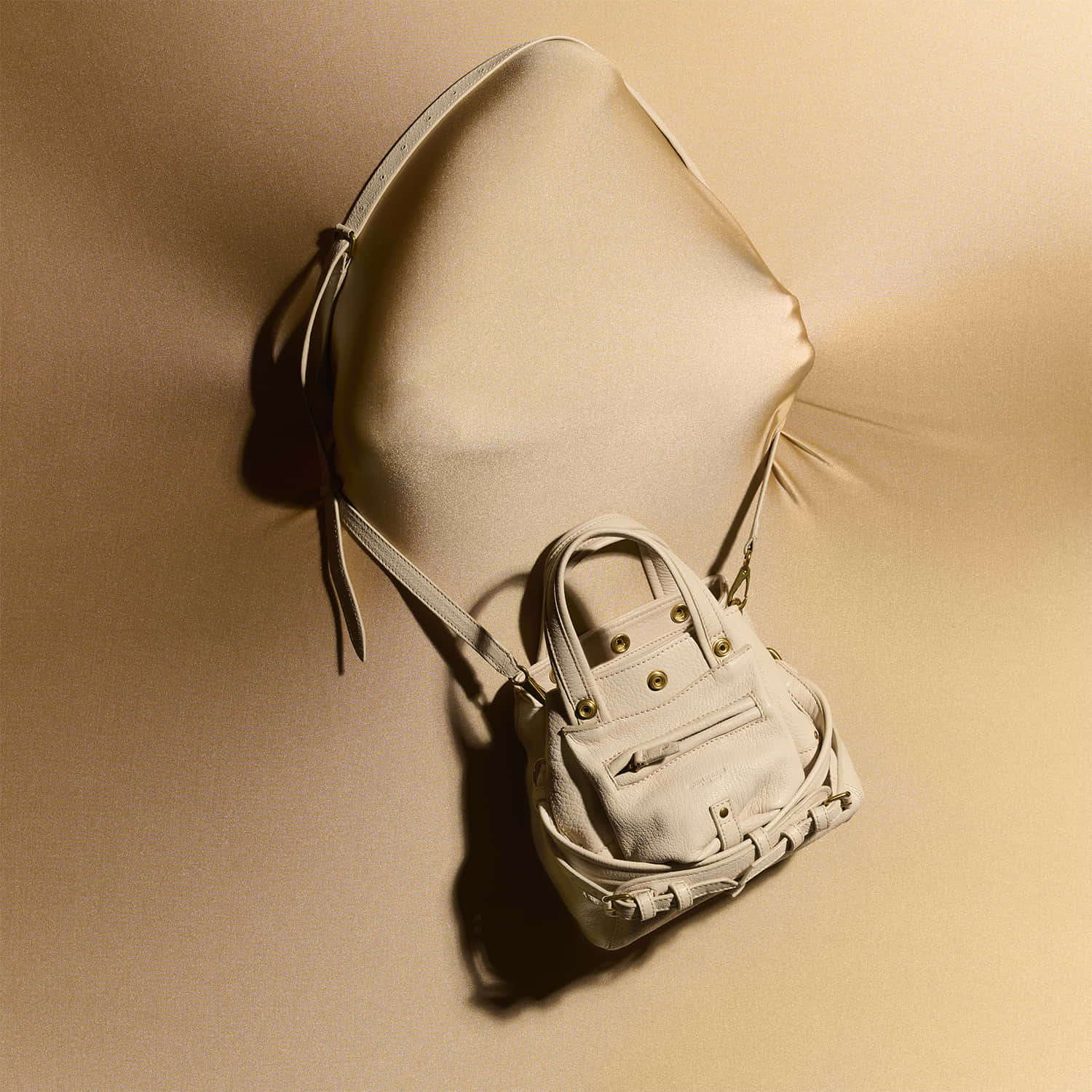 Handbag 桌布 壁紙 — 一個奶油色皮革手袋配金色五金件，放置在溫暖定向燈光下的垂墜緞面表面上。
