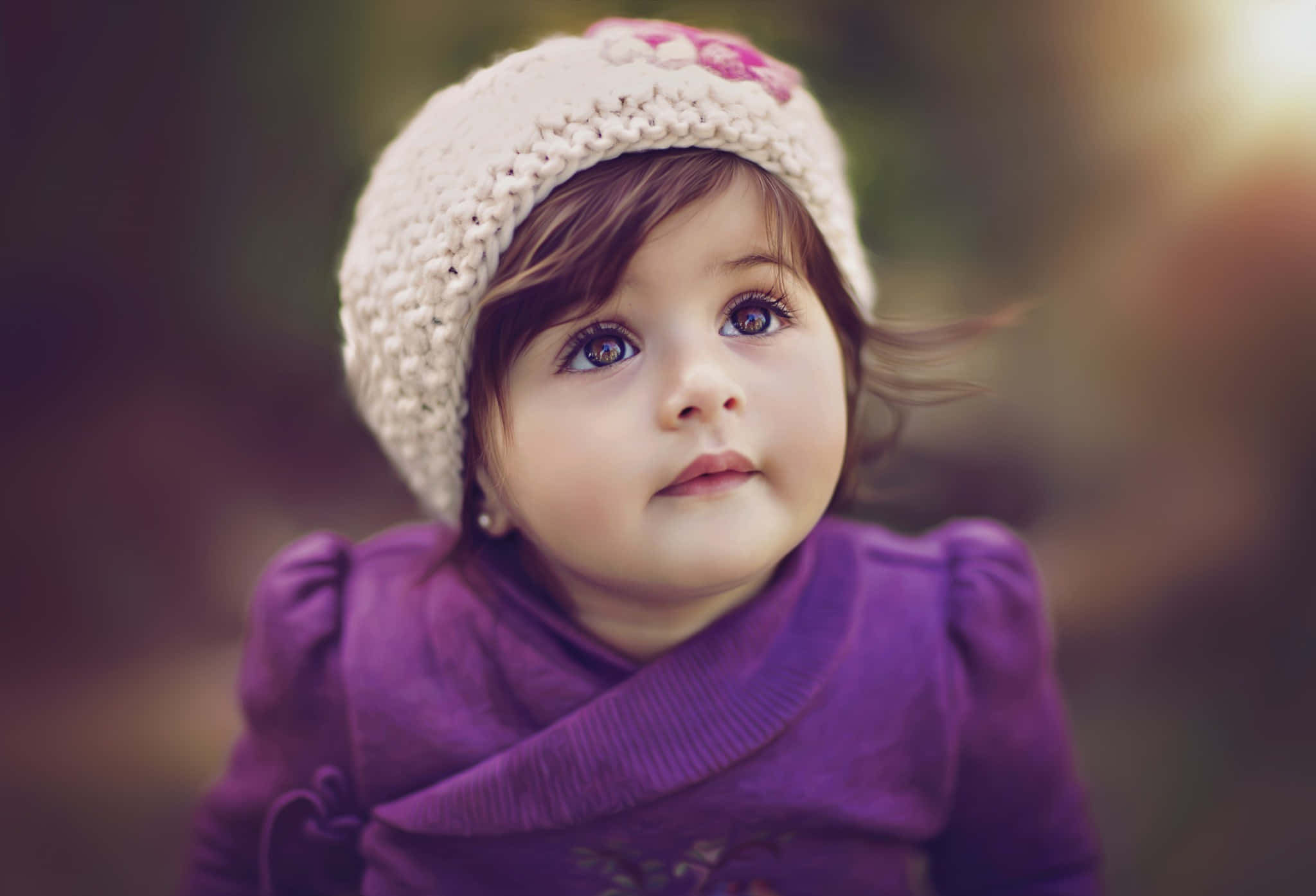 Baby Girl 桌布 壁紙 — 一個好奇幼兒的特寫，戴著奶油色針織帽和紫色毛衣，睜大眼睛向上凝視。