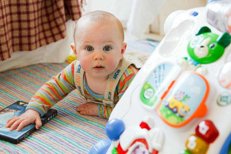 Baby Boy 桌布 壁紙 — 一個好奇的嬰兒穿著條紋衣服，在色彩繽紛的條紋毯子上爬行，旁邊有玩具和DVD。