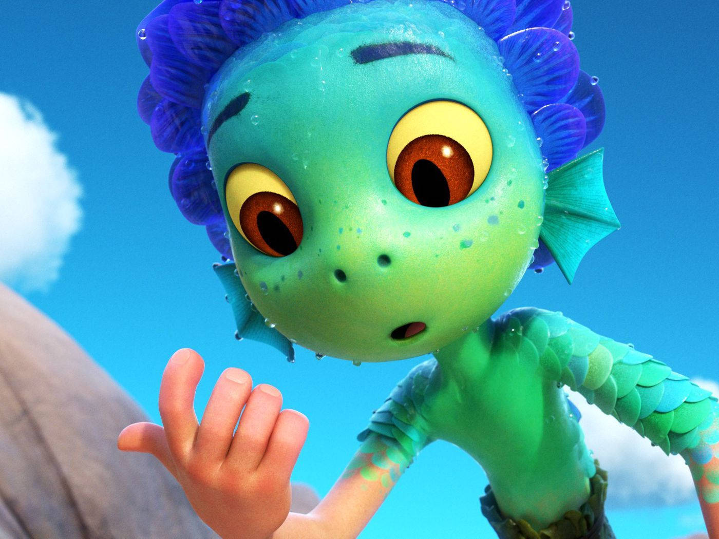 Pixar Luca 桌布 壁紙 — 一個好奇的綠色動畫人魚小孩，藍色尖刺頭髮和大棕色眼睛，在明亮的藍天下伸出手。