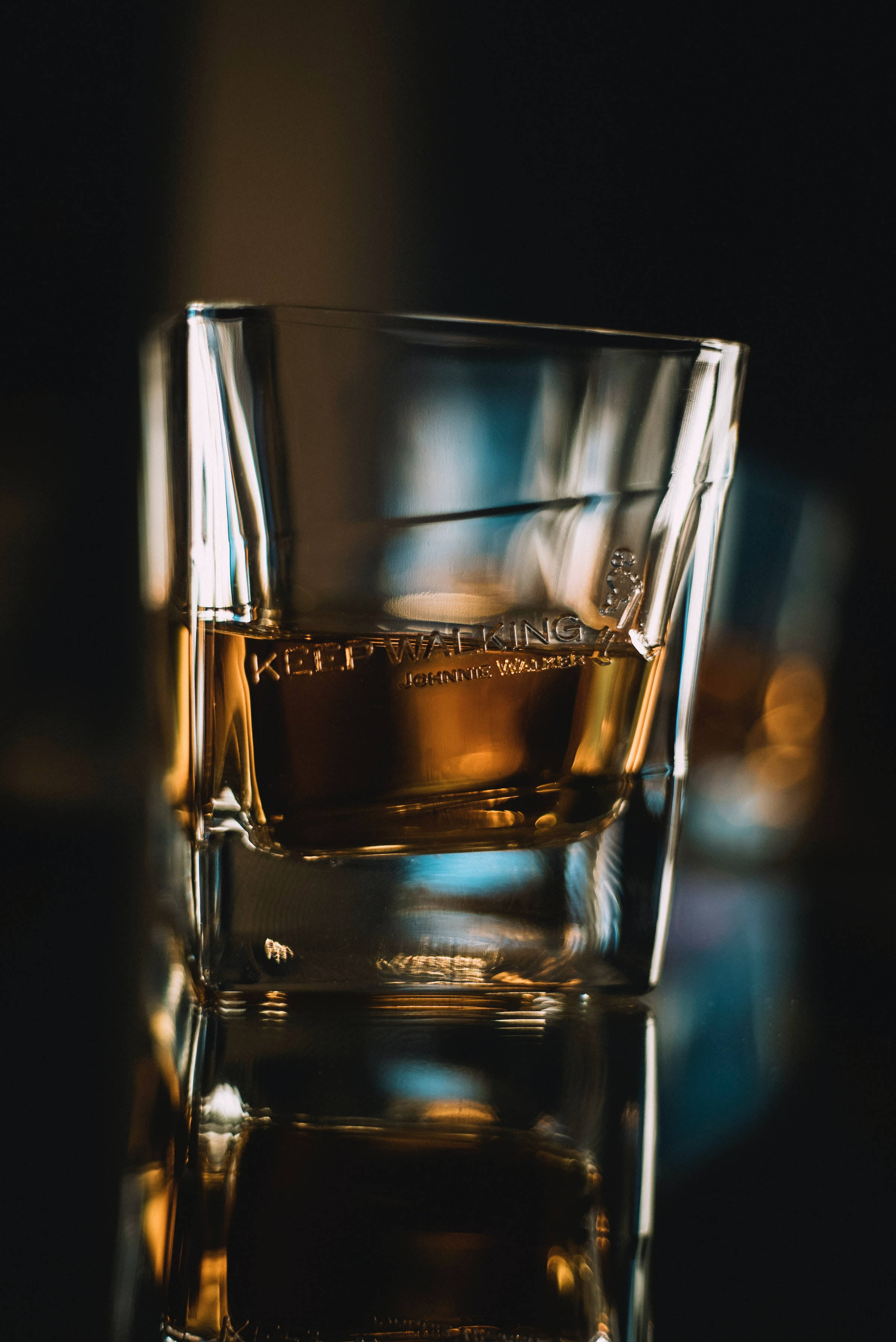 alcohol 桌布 壁紙 — 一個威士忌杯的特寫，杯上刻有 'KEEP WALKING'，在黑暗模糊的背景中溫暖地發光。