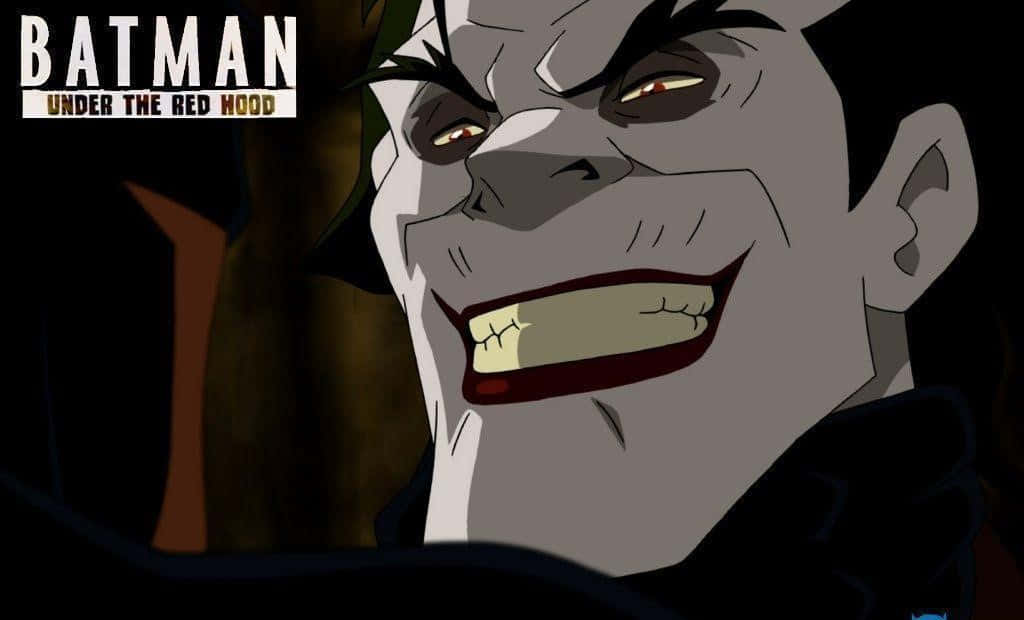 Batman Under The Red Hood 桌布 壁紙 — 一個威脅性的小丑特寫，咧嘴大笑，眼神銳利，處於黑暗的動畫場景中。