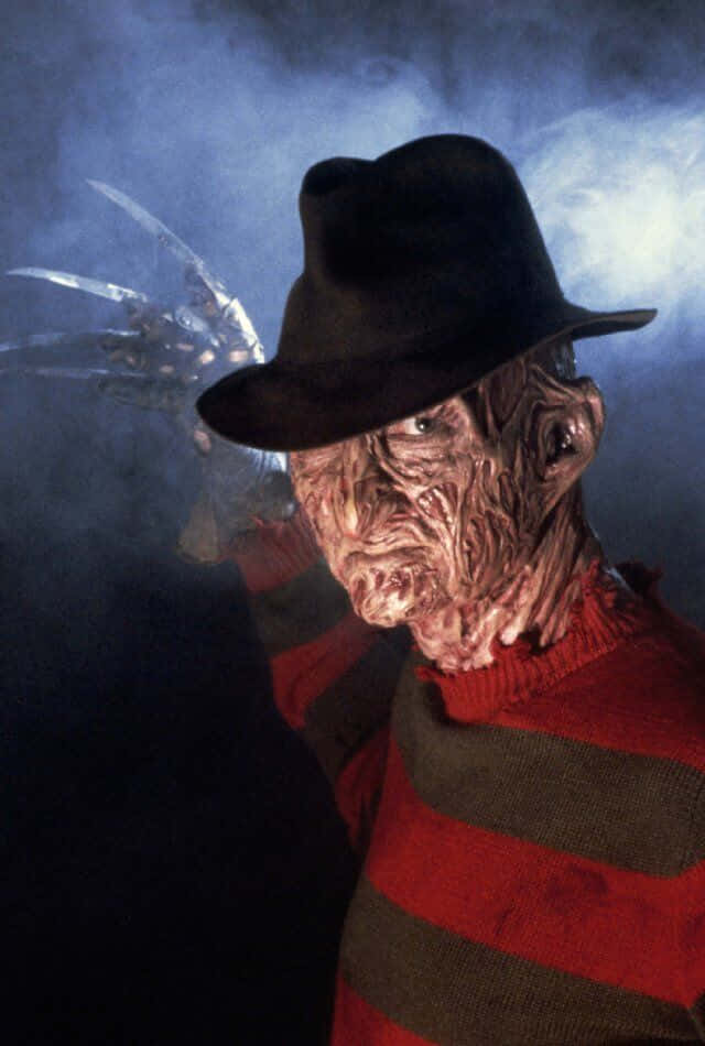 Freddy Krueger 桌布 壁紙 — 一個威脅性的弗雷迪·克魯格穿著他標誌性的條紋毛衣和軟呢帽，在煙霧繚繞的藍色背景下舉起他的利刃手套。