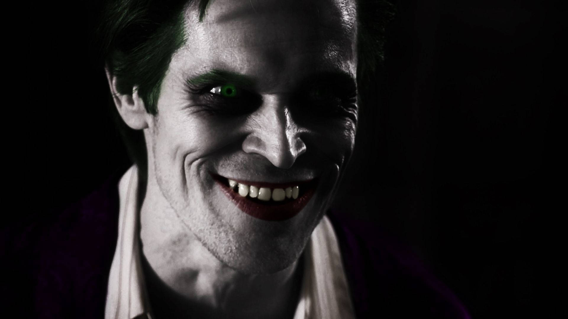Willem Dafoe 桌布 壁紙 — 一個威脅性的特寫鏡頭，小丑有一隻發光的綠色眼睛和一個寬闊的邪惡笑容，背景為黑色。