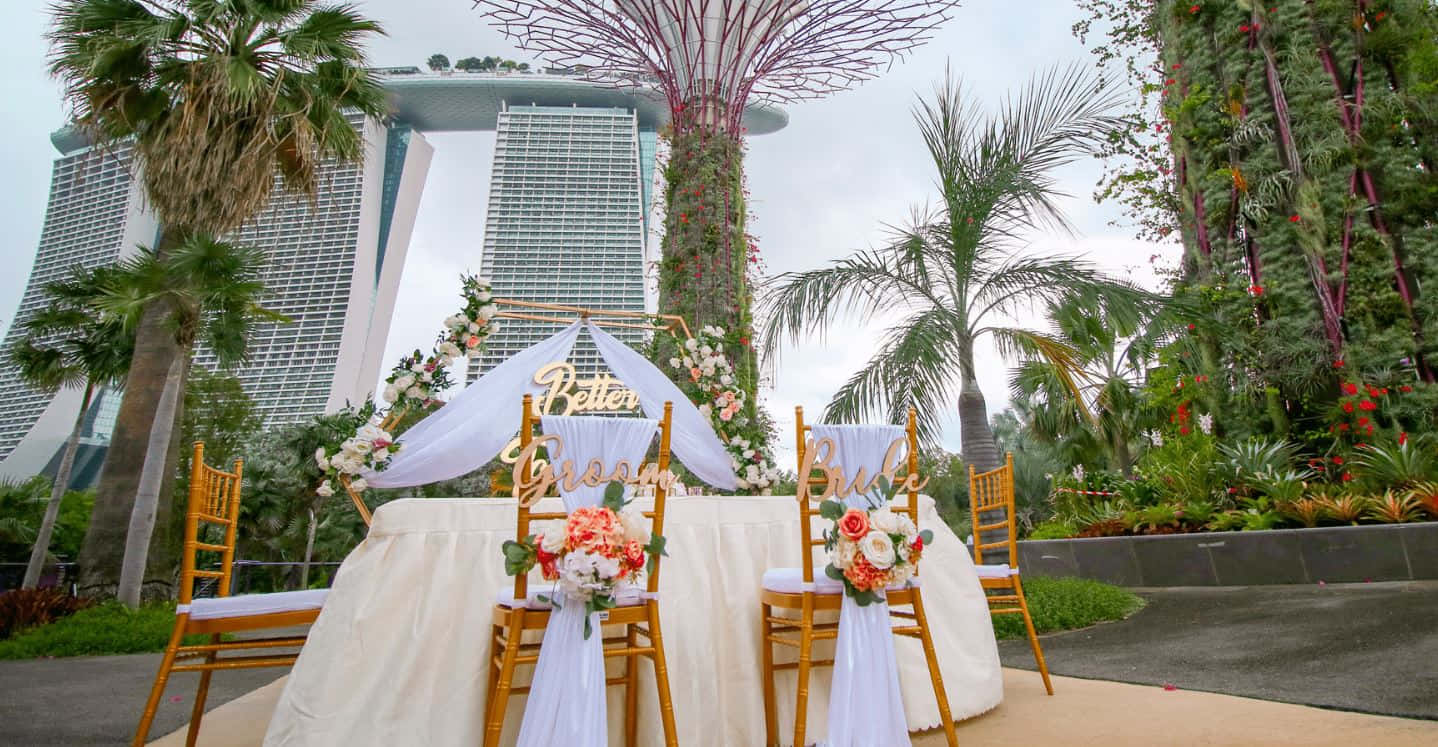 Garden Wedding 桌布 壁紙 — 一個婚禮祭壇，配有花卉佈置和木椅，以新加坡標誌性的濱海灣金沙和超級樹叢為背景。