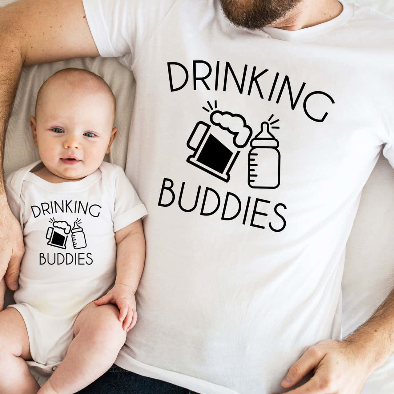 配對 桌布 壁紙 — 一個嬰兒和一個成年人穿著相配的「drinking buddies」T恤，上面有啤酒杯和瓶子圖案，在床上依偎。