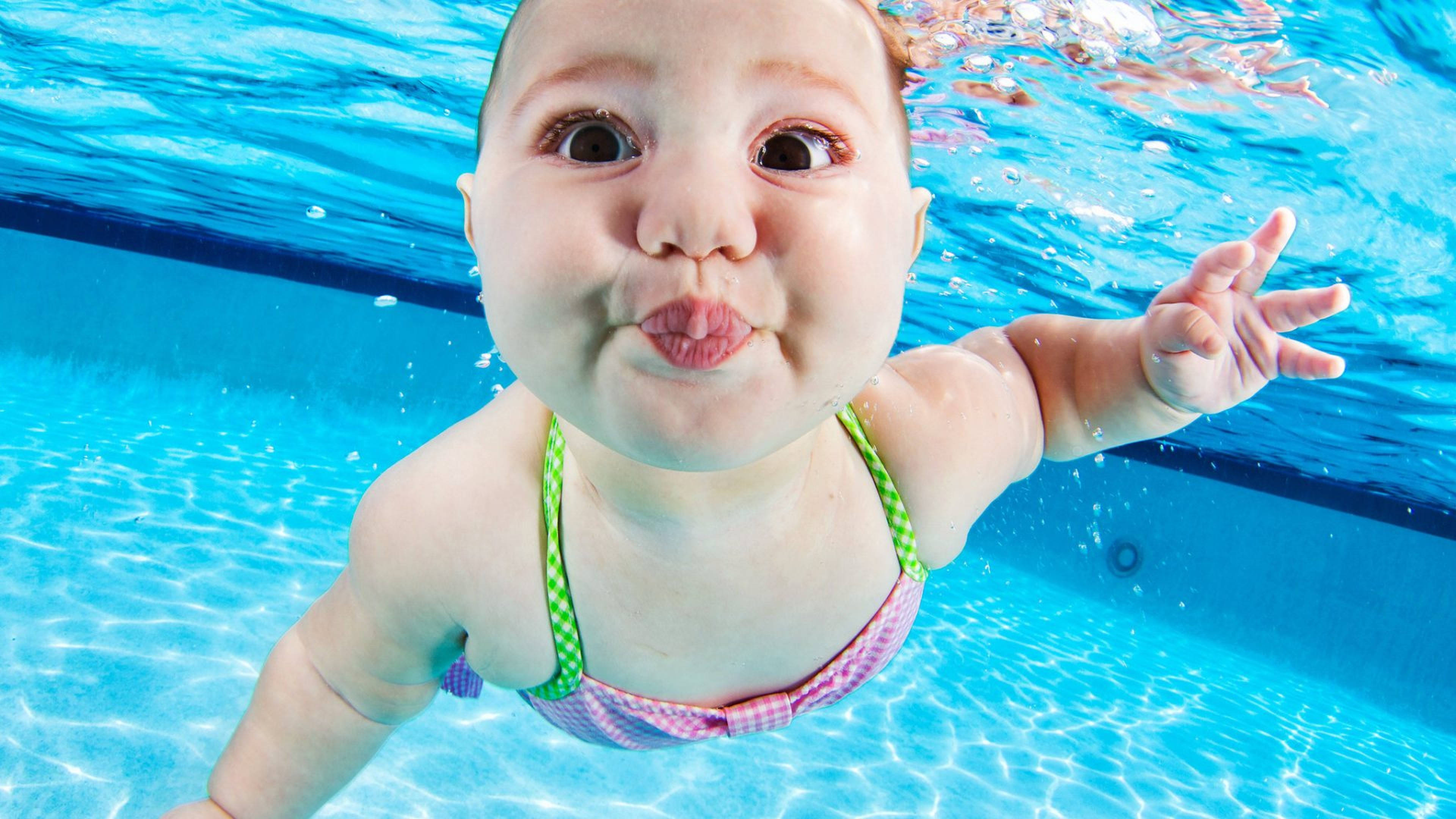 Swimming 桌布 壁紙 — 一個嬰兒在泳池水下做出一個俏皮的親親臉，周圍有明亮的藍色水波紋。