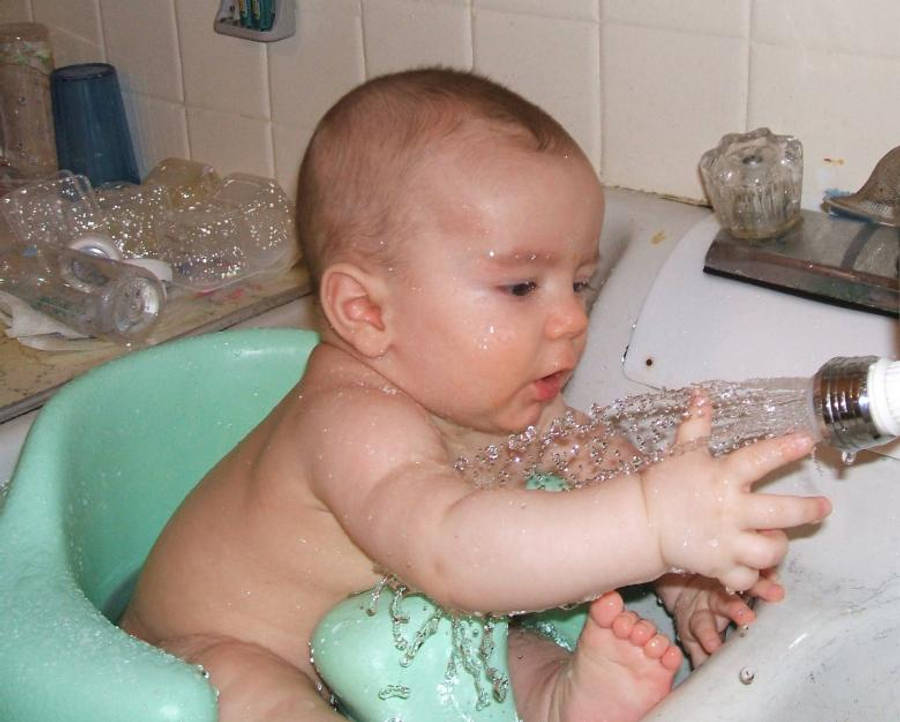 Baby Boy 桌布 壁紙 — 一個嬰兒在綠色浴椅上頑皮地握著瓷磚洗手台中正在流水的水龍頭。