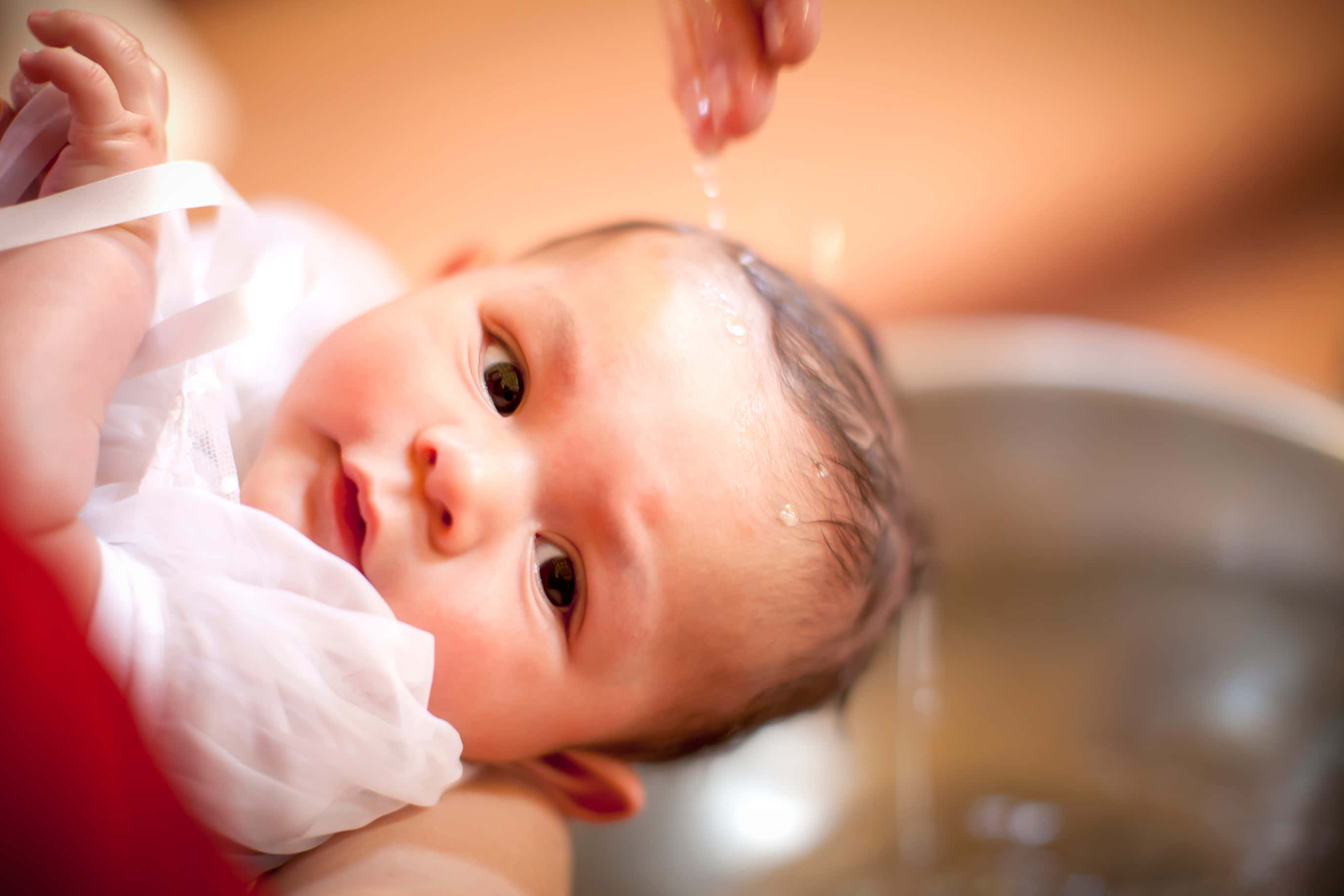 Baptism 桌布 壁紙 — 一個嬰兒正在被溫柔地洗澡，水滴落在他們的頭部和臉部的特寫。