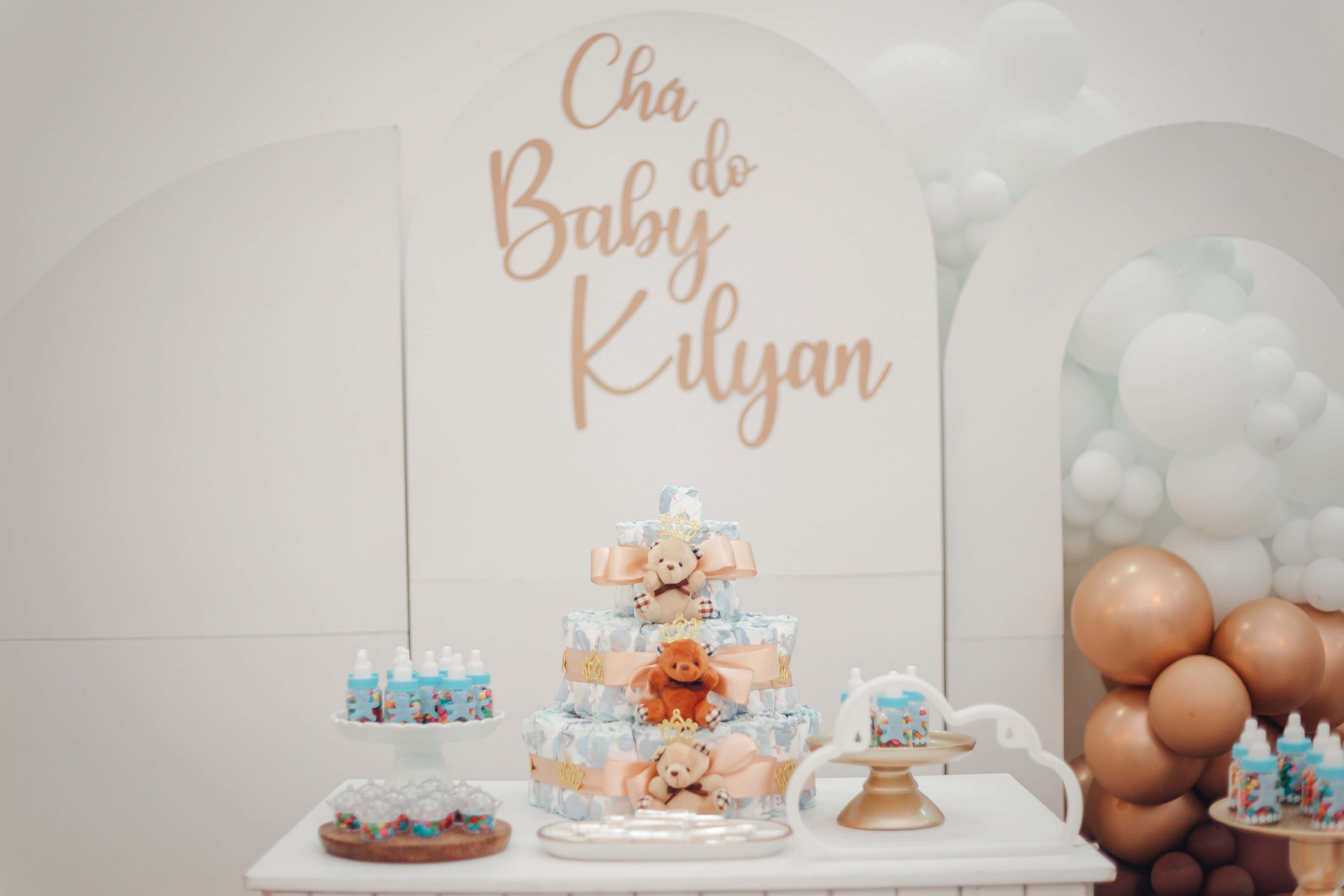Baby Shower 桌布 壁紙 — 一個嬰兒派對佈置，有一個尿布蛋糕，上面有泰迪熊，周圍環繞著金色和白色的氣球。