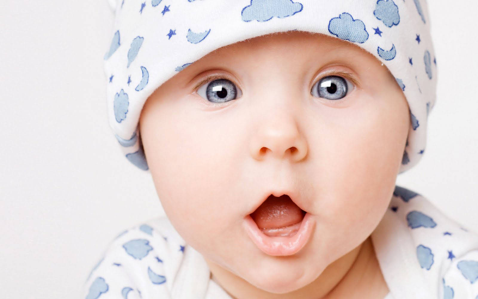 toddler 桌布 壁紙 — 一個嬰兒的特寫，有大大的藍色眼睛和張開的嘴巴，戴著藍色雲圖案帽子。