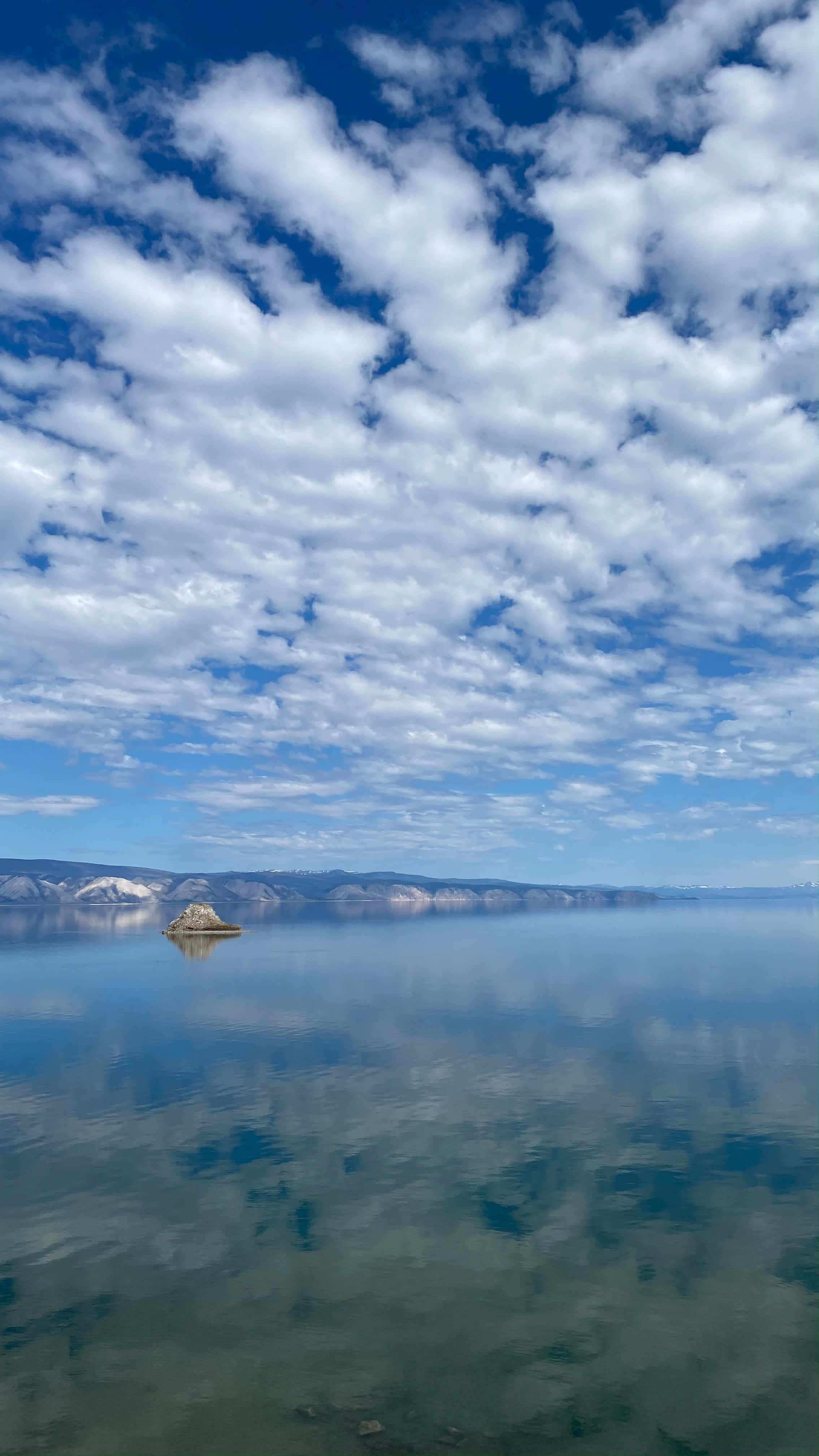 Lake 桌布 壁紙 — 一個孤島位於廣闊平靜的湖中央，倒映著明亮的藍天和蓬鬆的白雲。