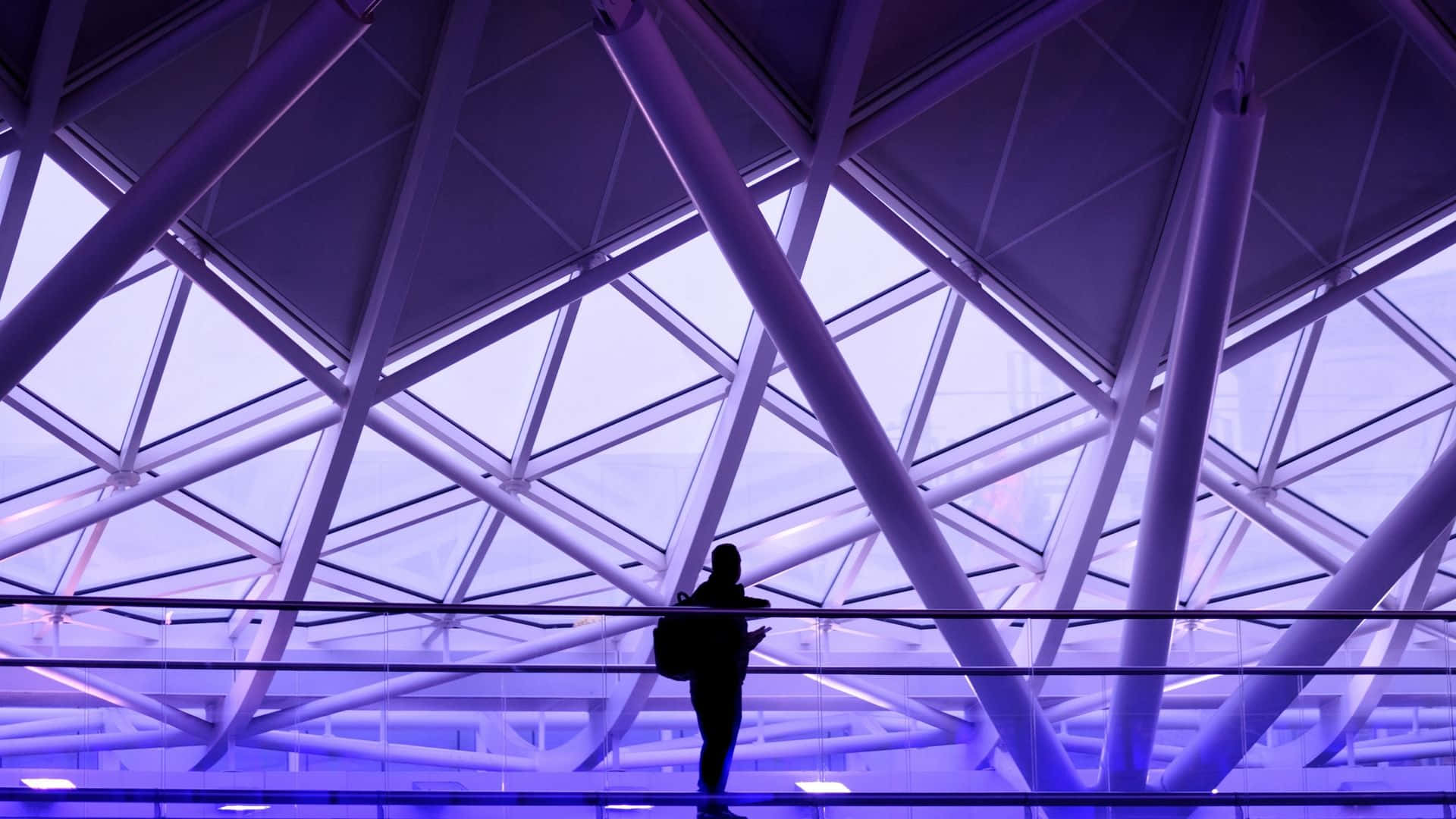 Minimalist Purple 桌布 壁紙 — 一個孤獨旅行者的剪影站在一個寬闊的幾何玻璃和鋼屋頂下，沐浴在冷紫色光中。