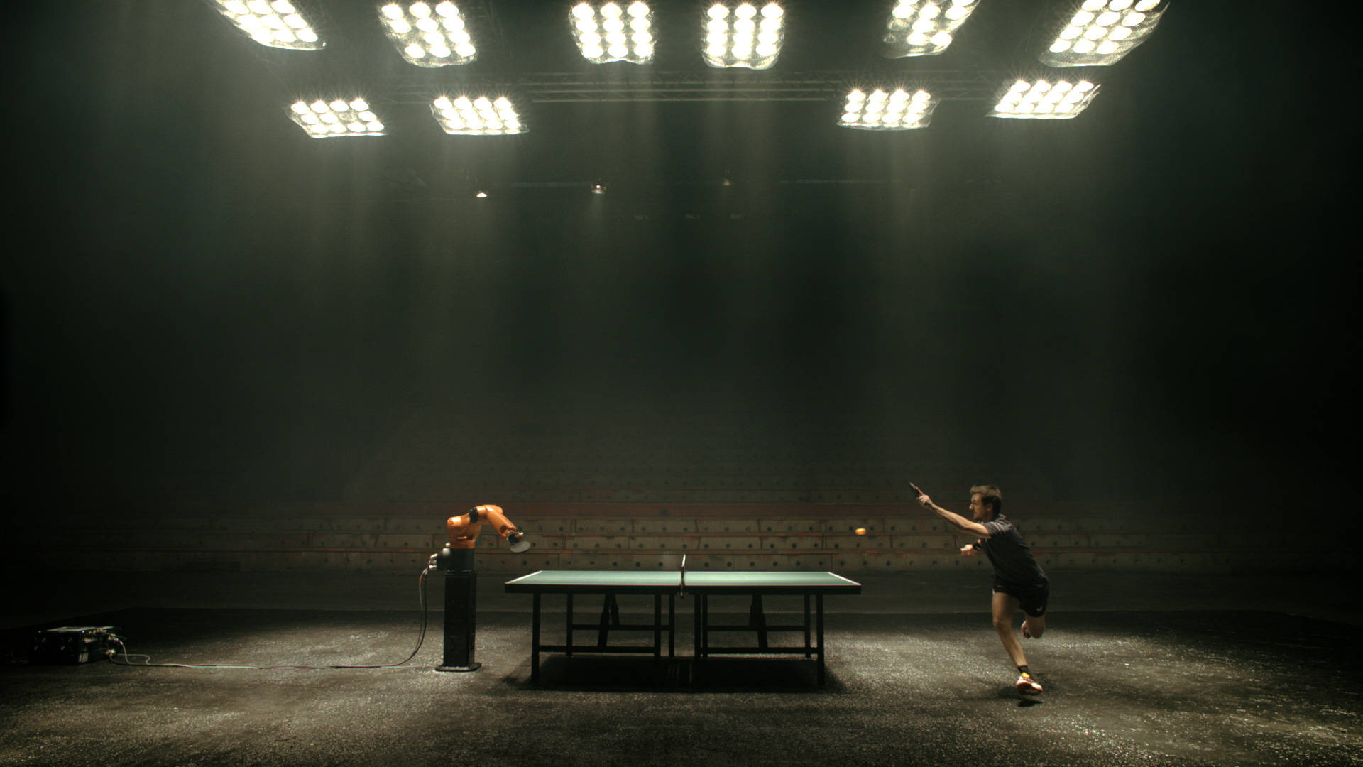 Table Tennis 桌布 壁紙 — 一個孤獨的乒乓球運動員在空蕩蕩的體育館中，在刺眼的球場燈光下，面對一個機器人對手。