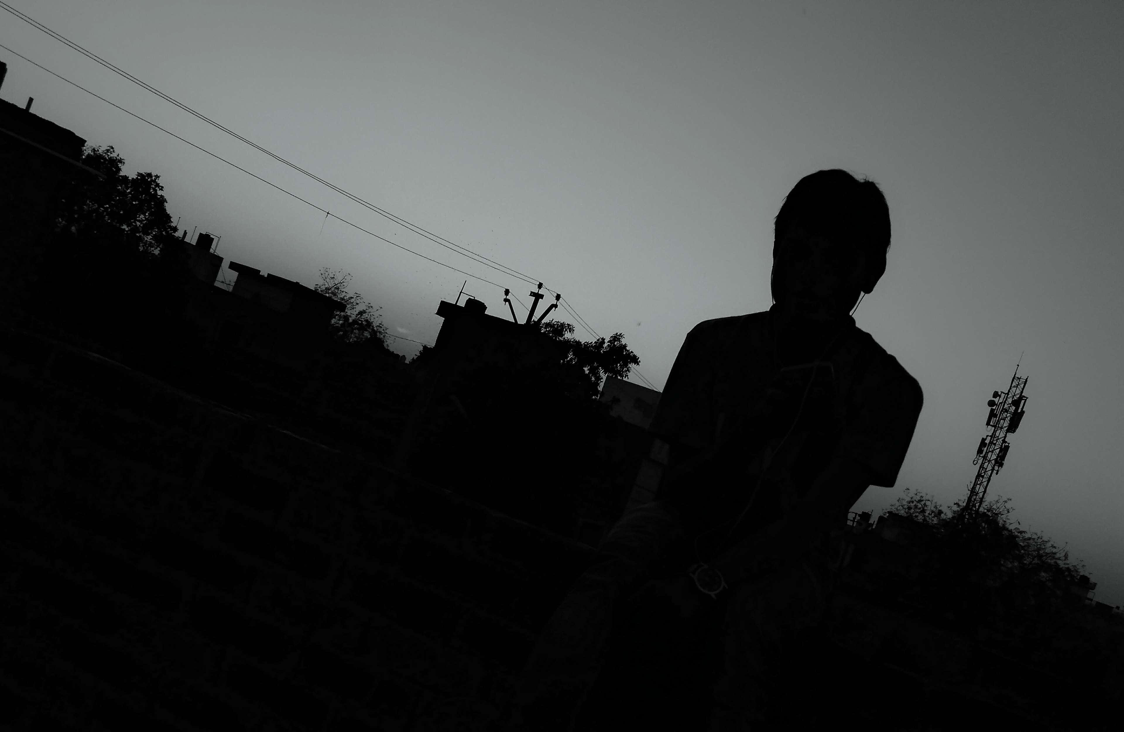 Dark Emotional 桌布 壁紙 — 一個孤獨的人以剪影形式站在昏暗的暮色天空下，背景是城市屋頂和電線。