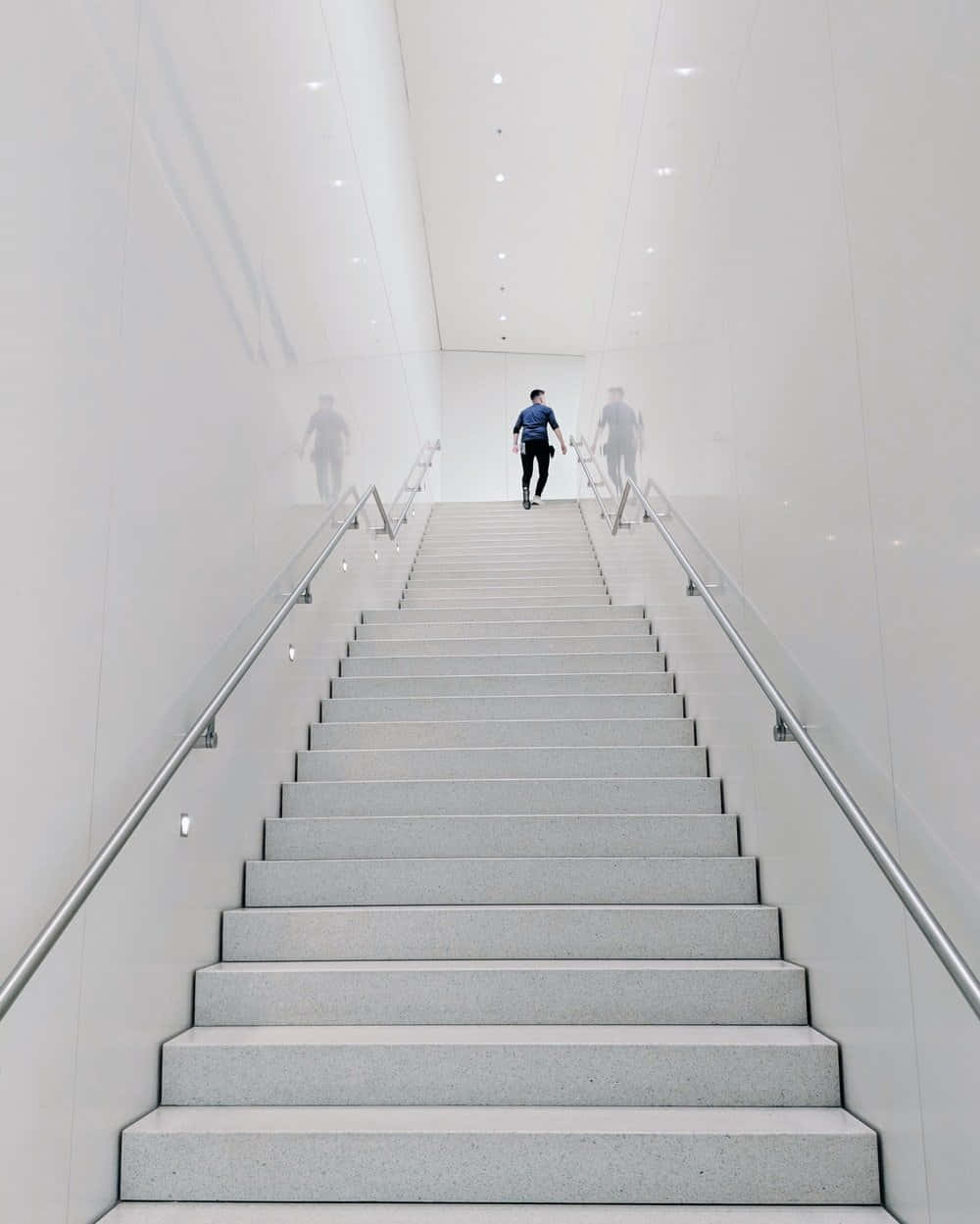 stairs 桌布 壁紙 — 一個孤獨的人在一間明亮白色現代室內空間中，走上長長的極簡樓梯，周圍是反射牆壁。