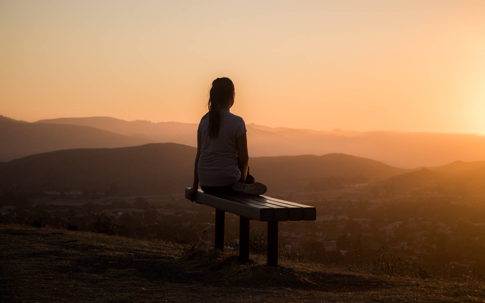 Alone 桌布 壁紙 — 一個孤獨的人坐在長椅上，在日落時分俯瞰沐浴在溫暖金色光芒中的連綿起伏的山丘。