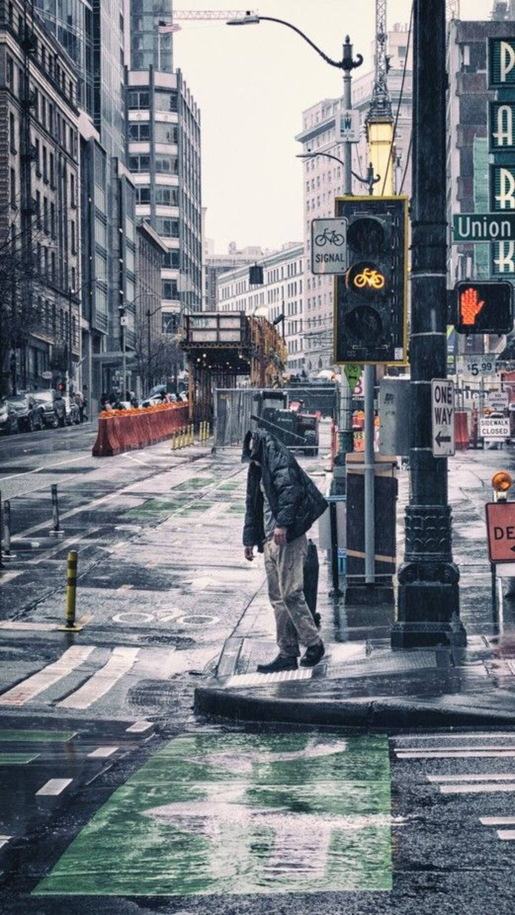 Rainy Day 桌布 壁紙 — 一個孤獨的人影在濕漉漉的城市街道上行走，頭頂是發光的黃色自行車號誌燈，雨水浸濕的路面反射著霓虹招牌。