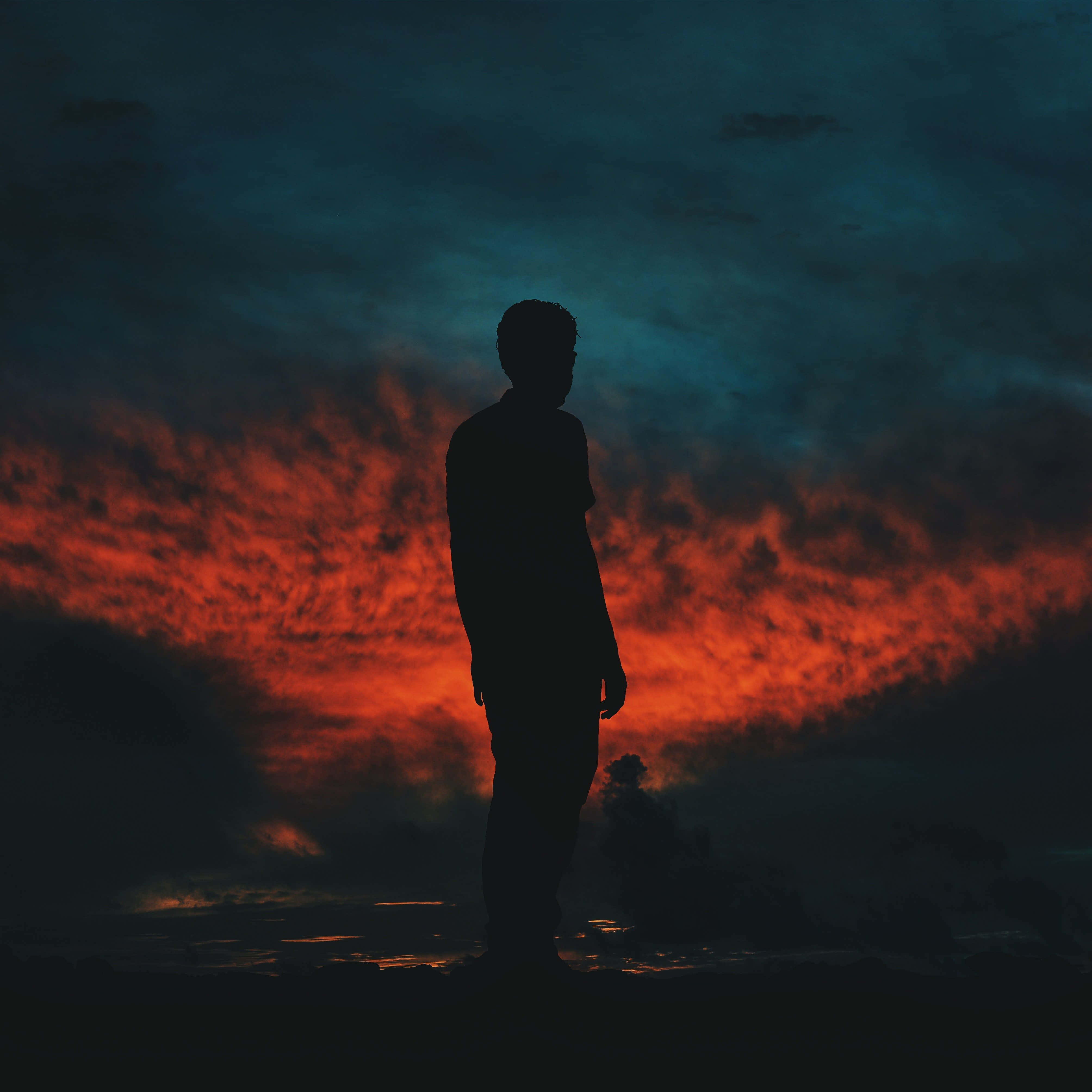 Silhouette 桌布 壁紙 — 一個孤獨的人影在黃昏時分，站在佈滿火紅橙色雲彩的戲劇性天空下。