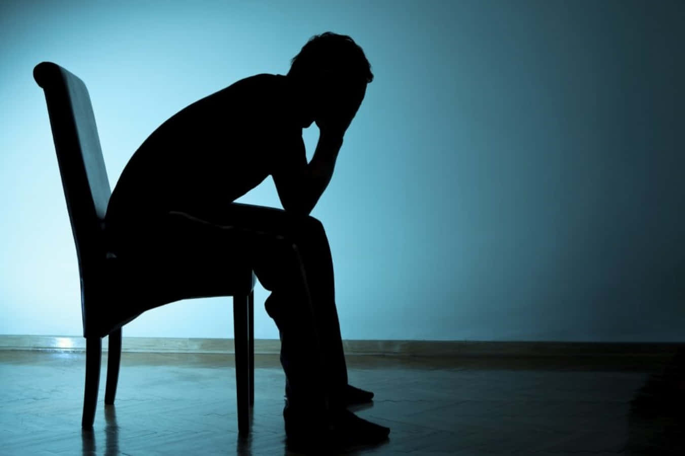 Alone 桌布 壁紙 — 一個孤獨的人影癱坐在椅子上，雙手抱頭，靠著微暗房間裡清涼的藍色牆壁。