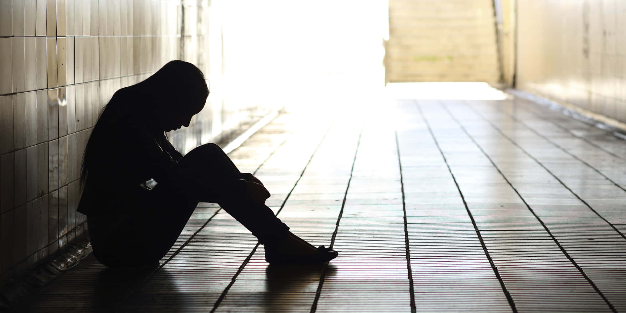 Lonely 桌布 壁紙 — 一個孤獨的人影蜷縮在瓷磚地板上，身處昏暗的隧道中，前方出口有明亮的光線湧入。
