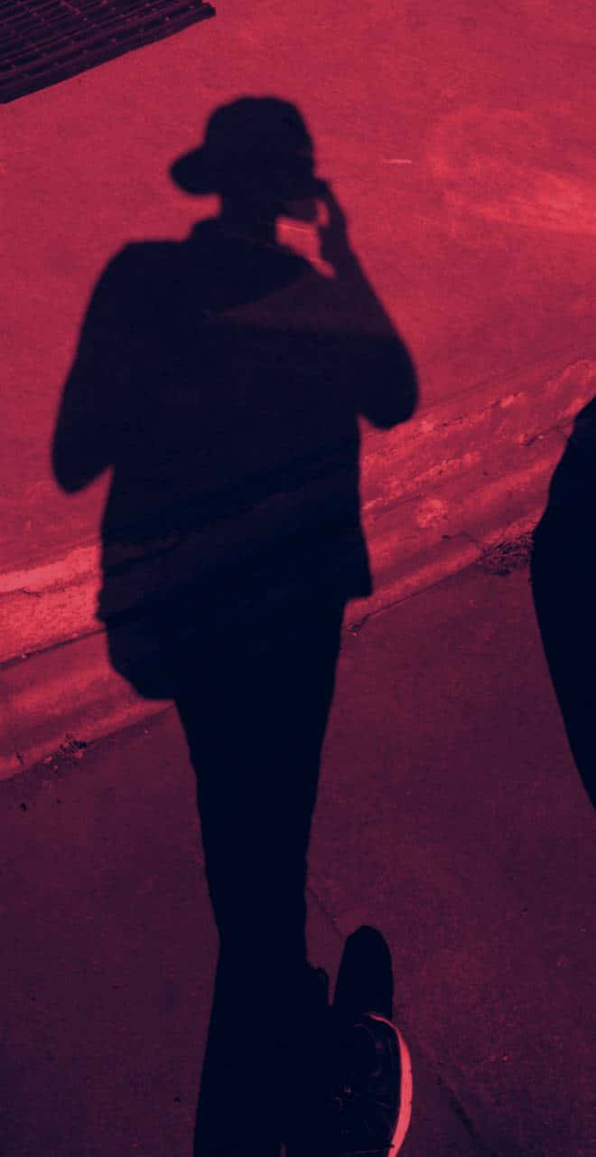 Silhouette 桌布 壁紙 — 一個孤獨的人的剪影，走在一條沐浴在強烈紅光中、投下長長陰影的街道上。