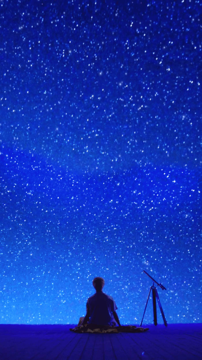 Stars 桌布 壁紙 — 一個孤獨的人盤腿坐在木甲板上，頭頂是廣闊的星空，附近有一個望遠鏡。