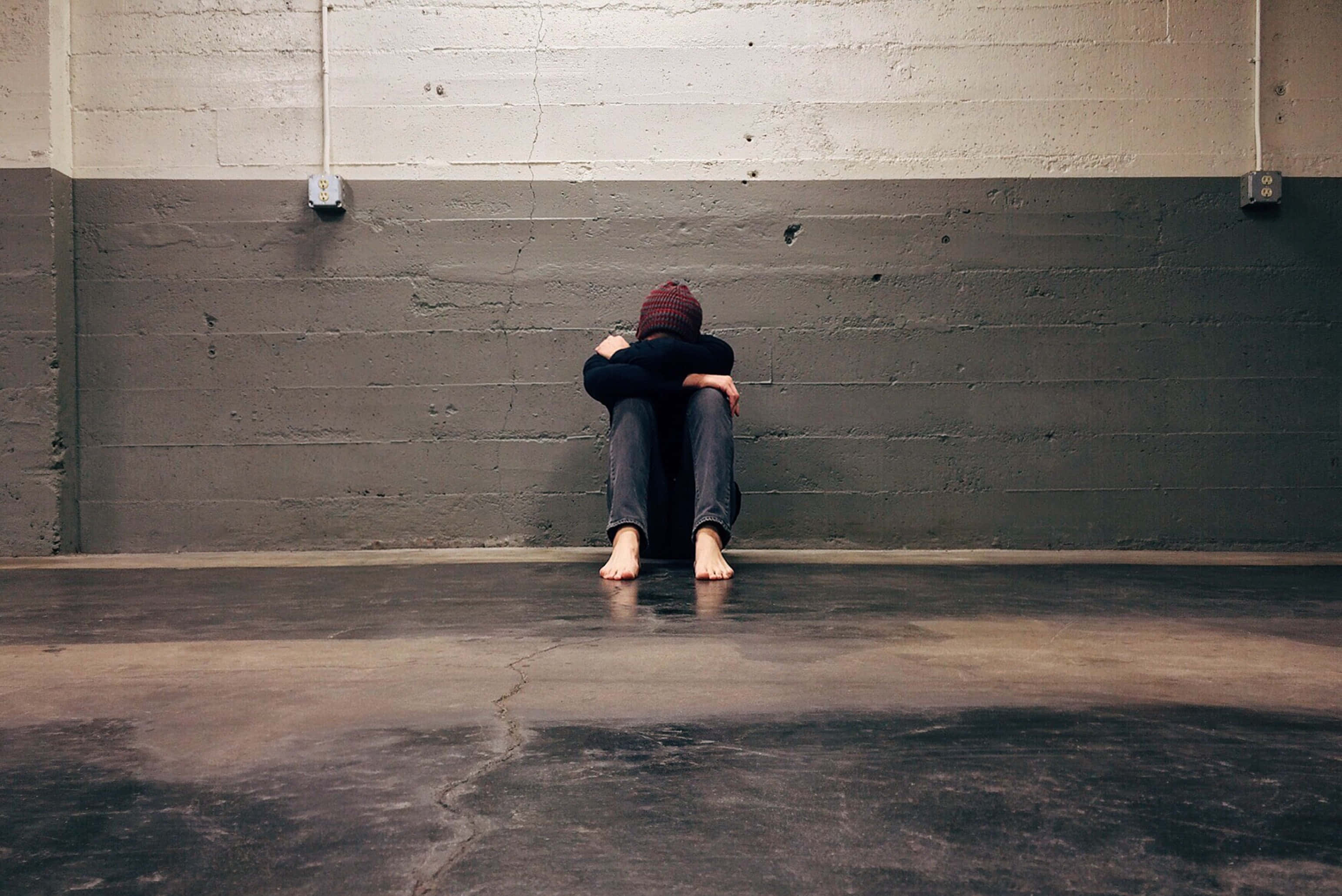 Alone Boy 桌布 壁紙 — 一個孤獨的人蜷縮在裂開的混凝土牆邊，身處一個空蕩蕩的工業空間。