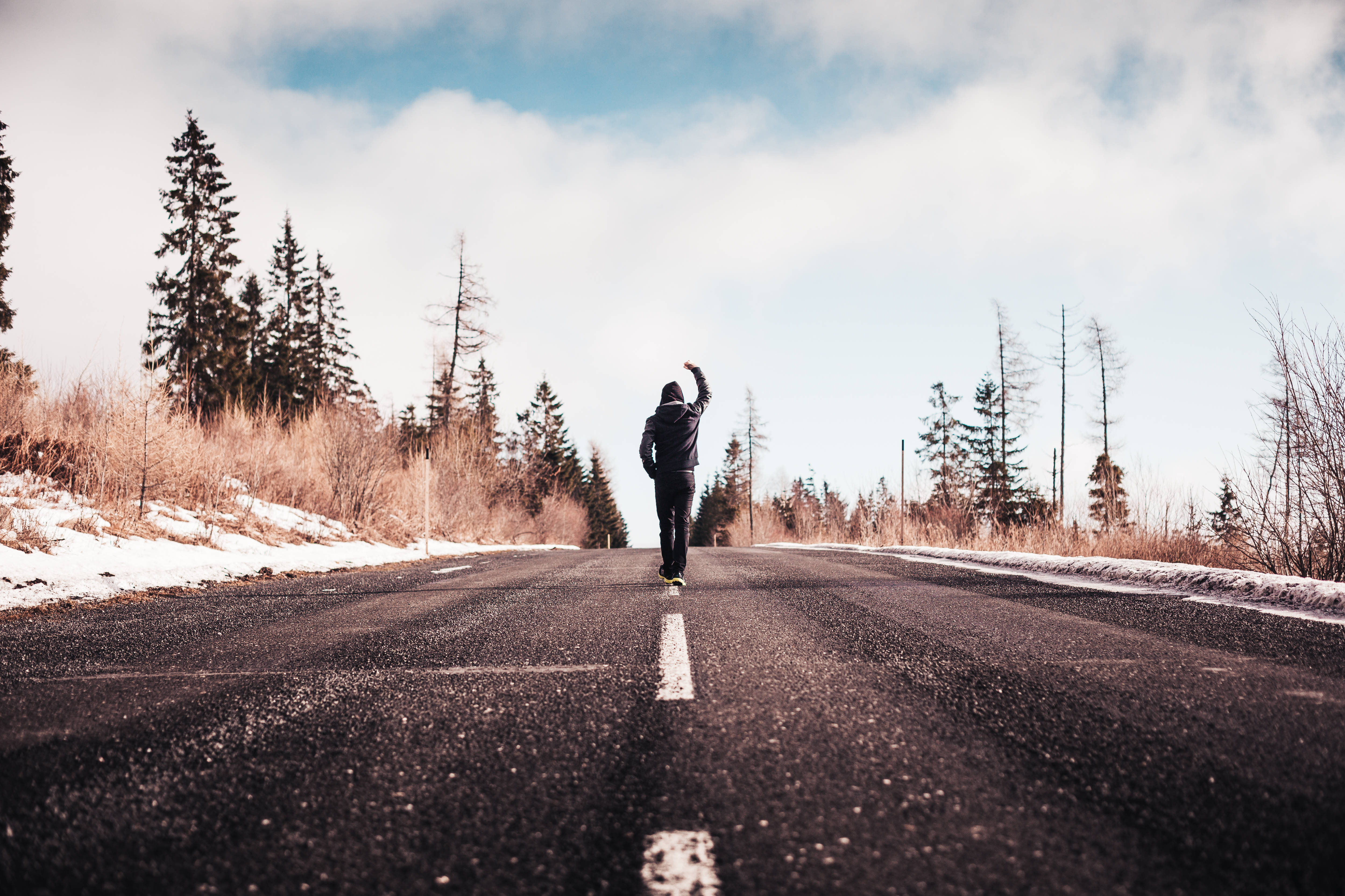 Motivation 桌布 壁紙 — 一個孤獨的人走在積雪的森林道路上，向多雲的天空舉起一隻手臂。
