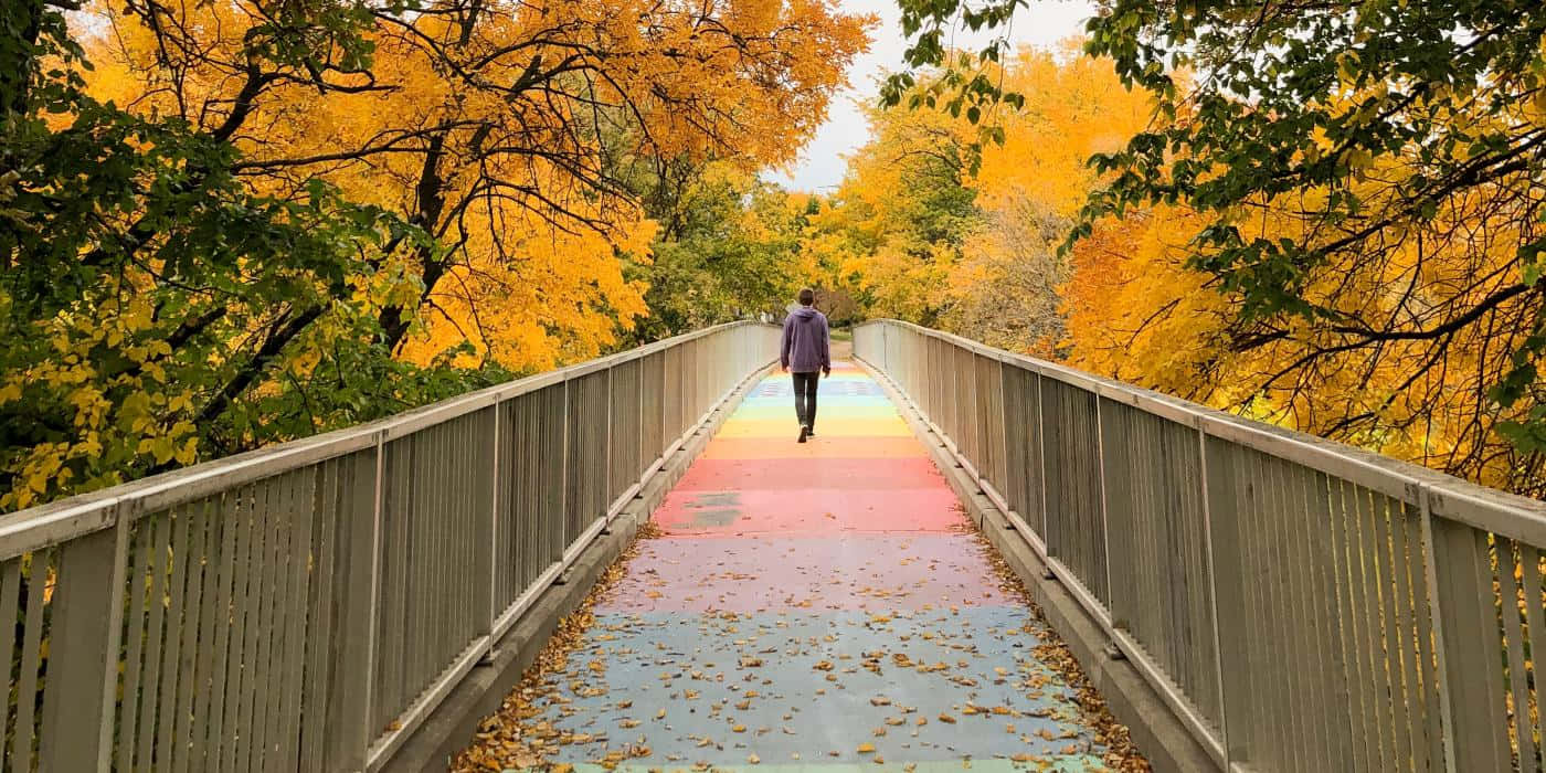 Fall Bridge 桌布 壁紙 — 一個孤獨的人走過一條色彩繽紛的彩虹色行人天橋，四周環繞著金黃色的秋葉。