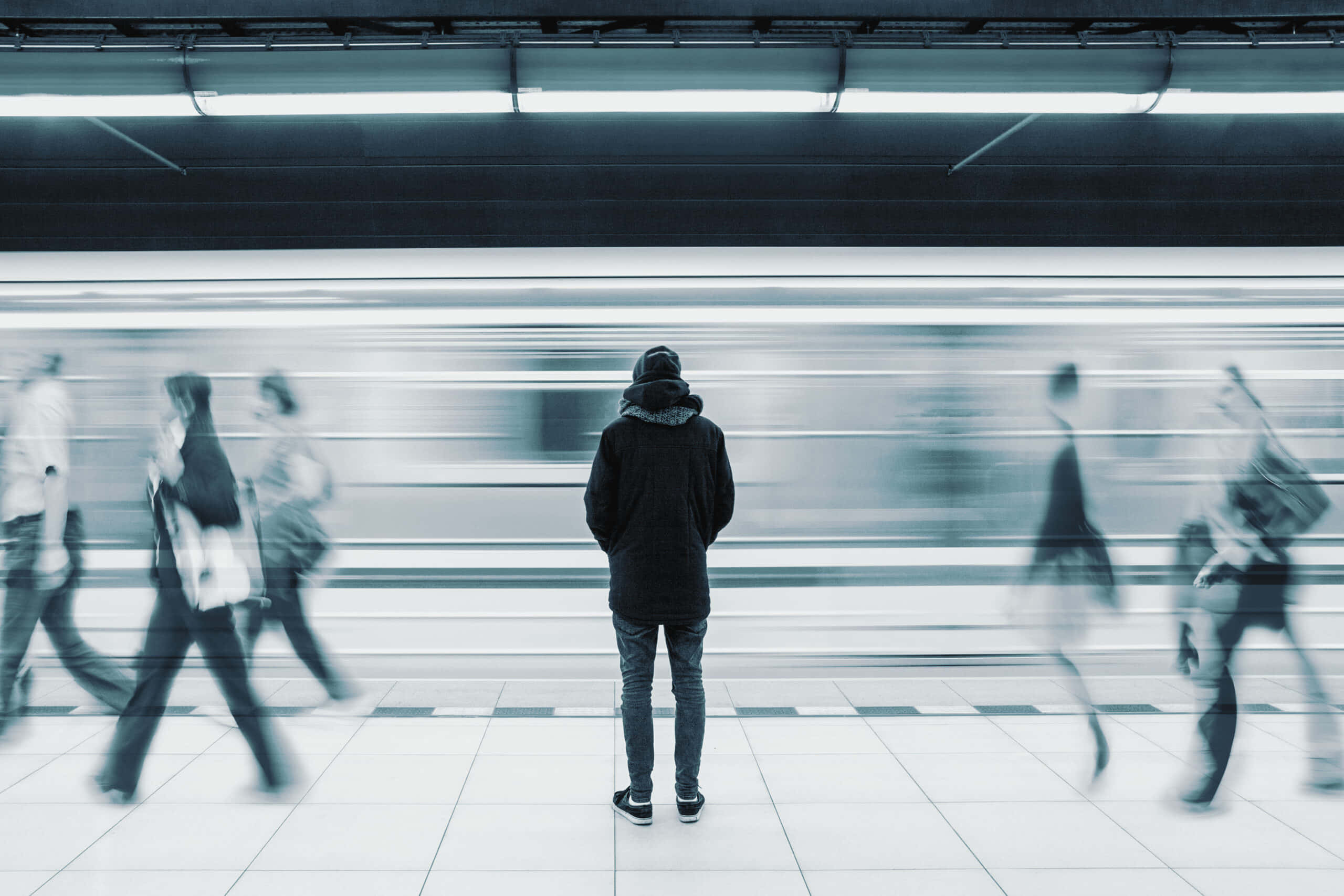 Alone 桌布 壁紙 — 一個孤獨的人靜靜地站在地鐵月台上，模糊的人群和列車在清冷的藍色單色場景中疾馳而過。