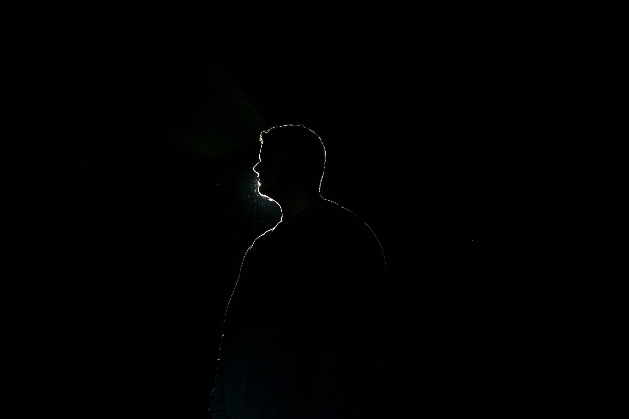 Silhouette 桌布 壁紙 — 一個孤獨的人類剪影站在深邃的黑暗中，一道光束從背後勾勒出他們的輪廓。