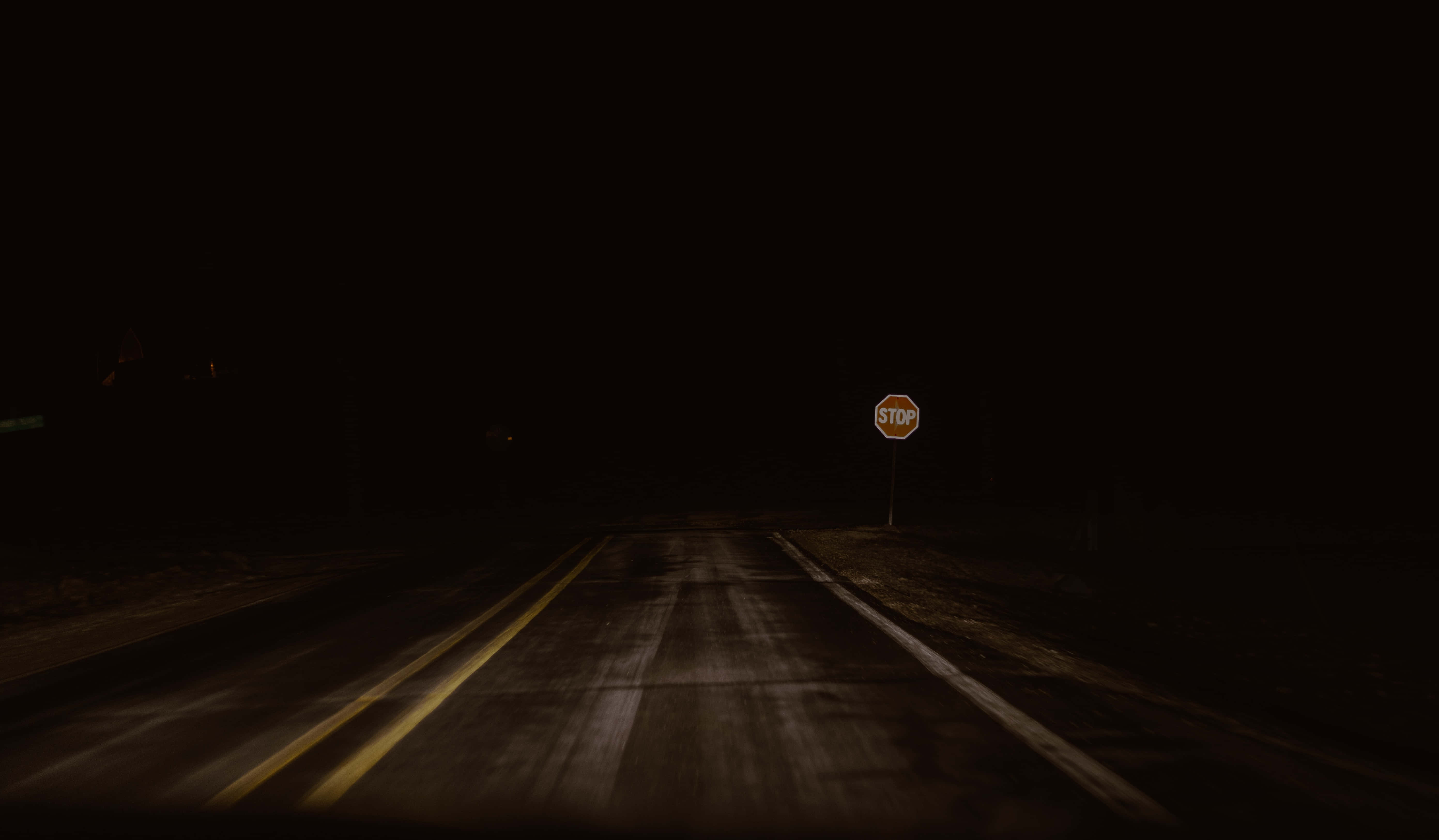 Dark Crossroad 桌布 壁紙 — 一個孤獨的停車標誌矗立在夜晚昏暗車燈照亮的黑暗空曠道路邊緣。