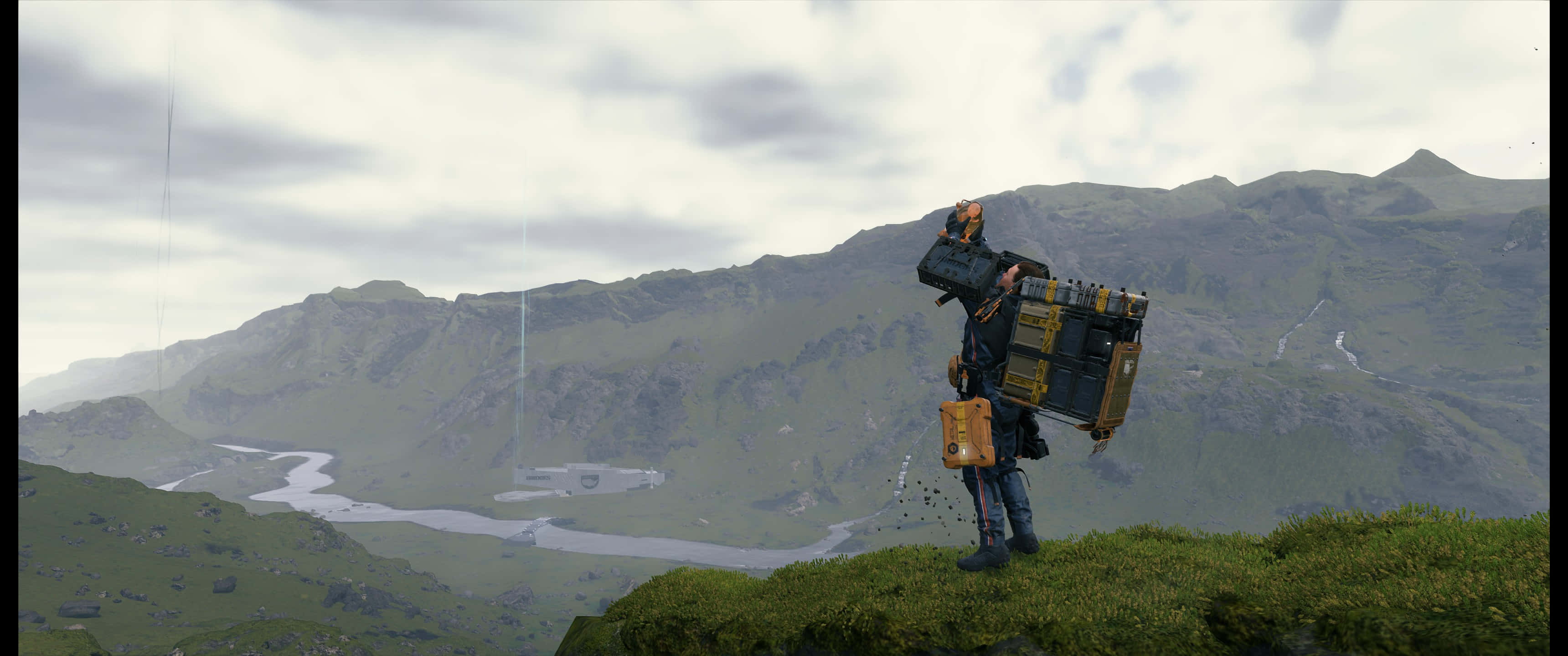 3440x1440p Death Stranding 桌布 壁紙 — 一個孤獨的冒險家站在長滿草的山脊上，背著一個沉重的未來風格背包，俯瞰蜿蜒的河谷。