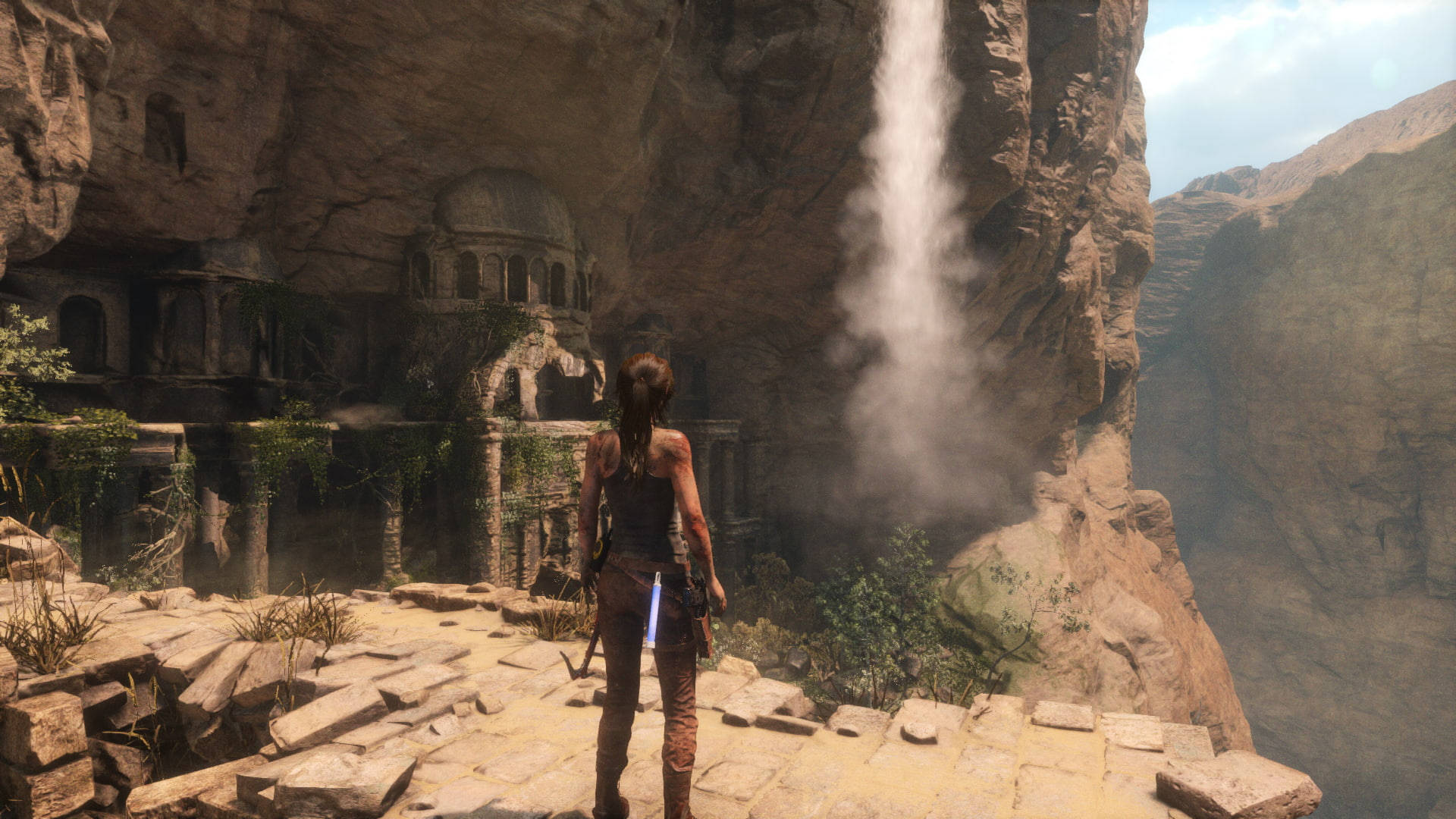 Rise Of The Tomb Raider 桌布 壁紙 — 一個孤獨的冒險家站在雄偉的瀑布前，瀑布在崎嶇峽谷中的古老遺跡旁傾瀉而下。