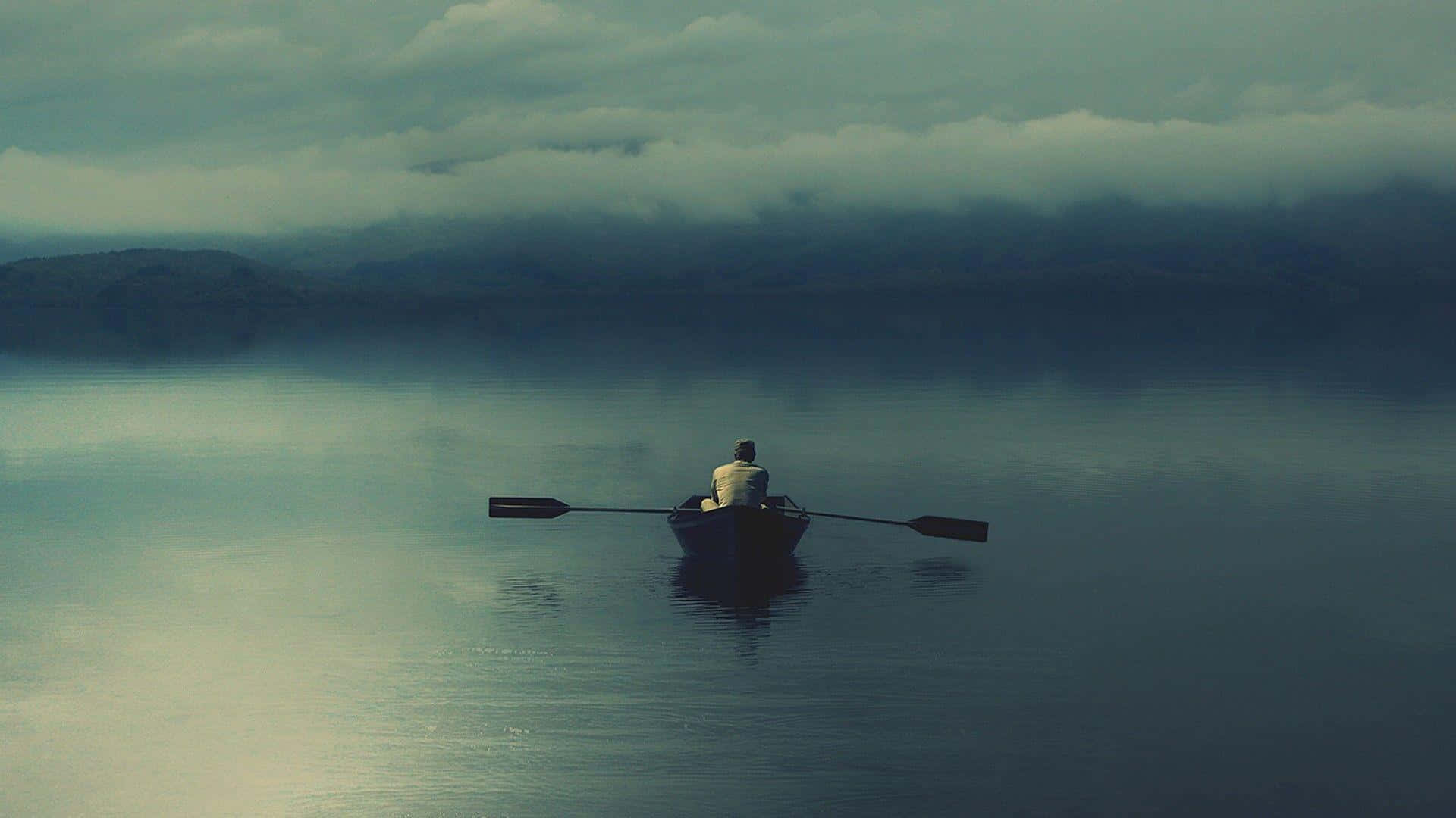 Lonely 桌布 壁紙 — 一個孤獨的划船者坐在小船裡，在雲霧繚繞的天空下，滑過霧氣瀰漫的湖泊，遠方的山丘幾乎看不見。