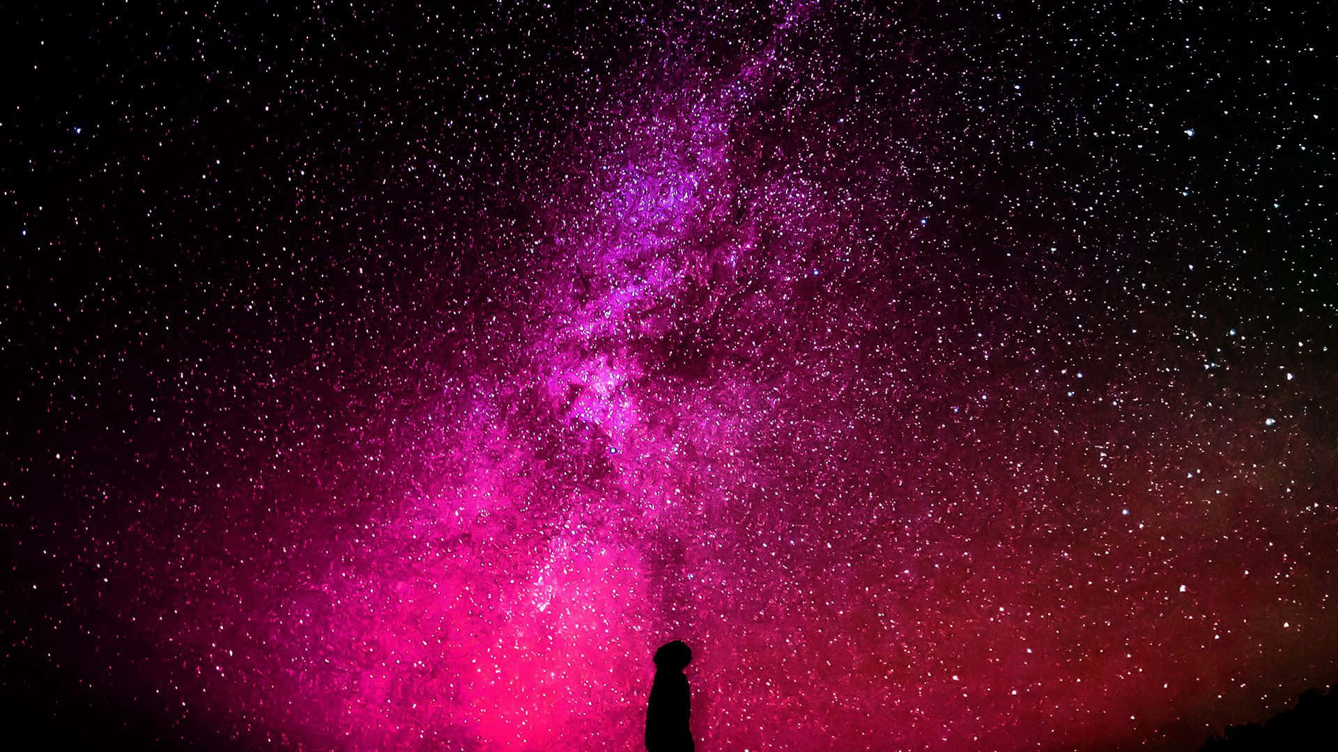 粉紅銀河 桌布 壁紙 — 一個孤獨的剪影仰望橫跨星空夜空的鮮豔粉紅和紫色星系。