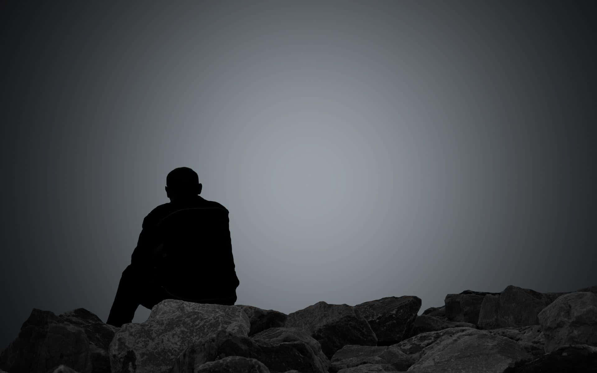 Silhouette 桌布 壁紙 — 一個孤獨的剪影坐在崎嶇的岩石上，凝視著廣闊的漸變天空。