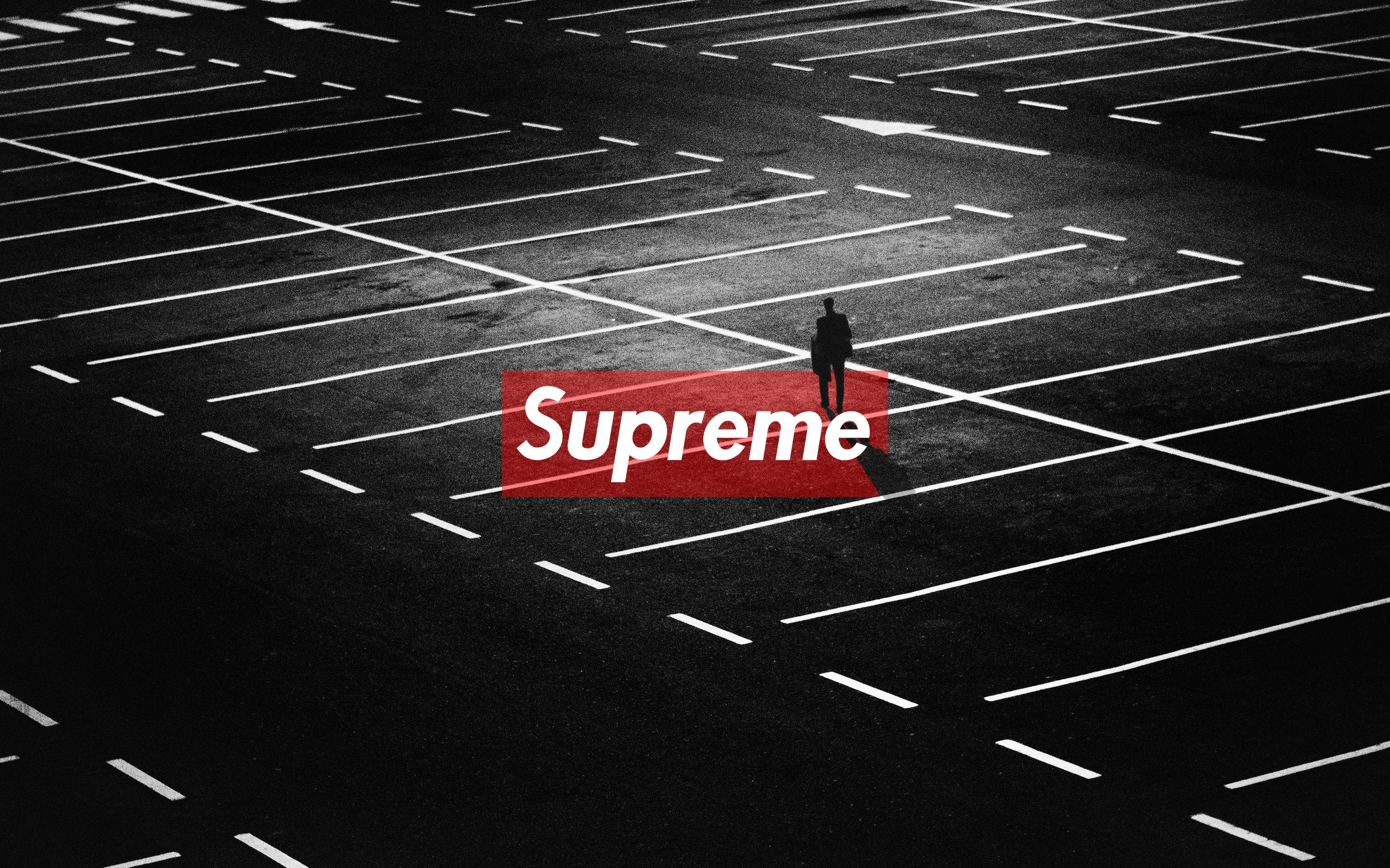 supreme 桌布 壁紙 — 一個孤獨的剪影站在廣闊的空蕩蕩的停車場中，在強烈的人造光下，帶有醒目的紅色Supreme標誌覆蓋層。