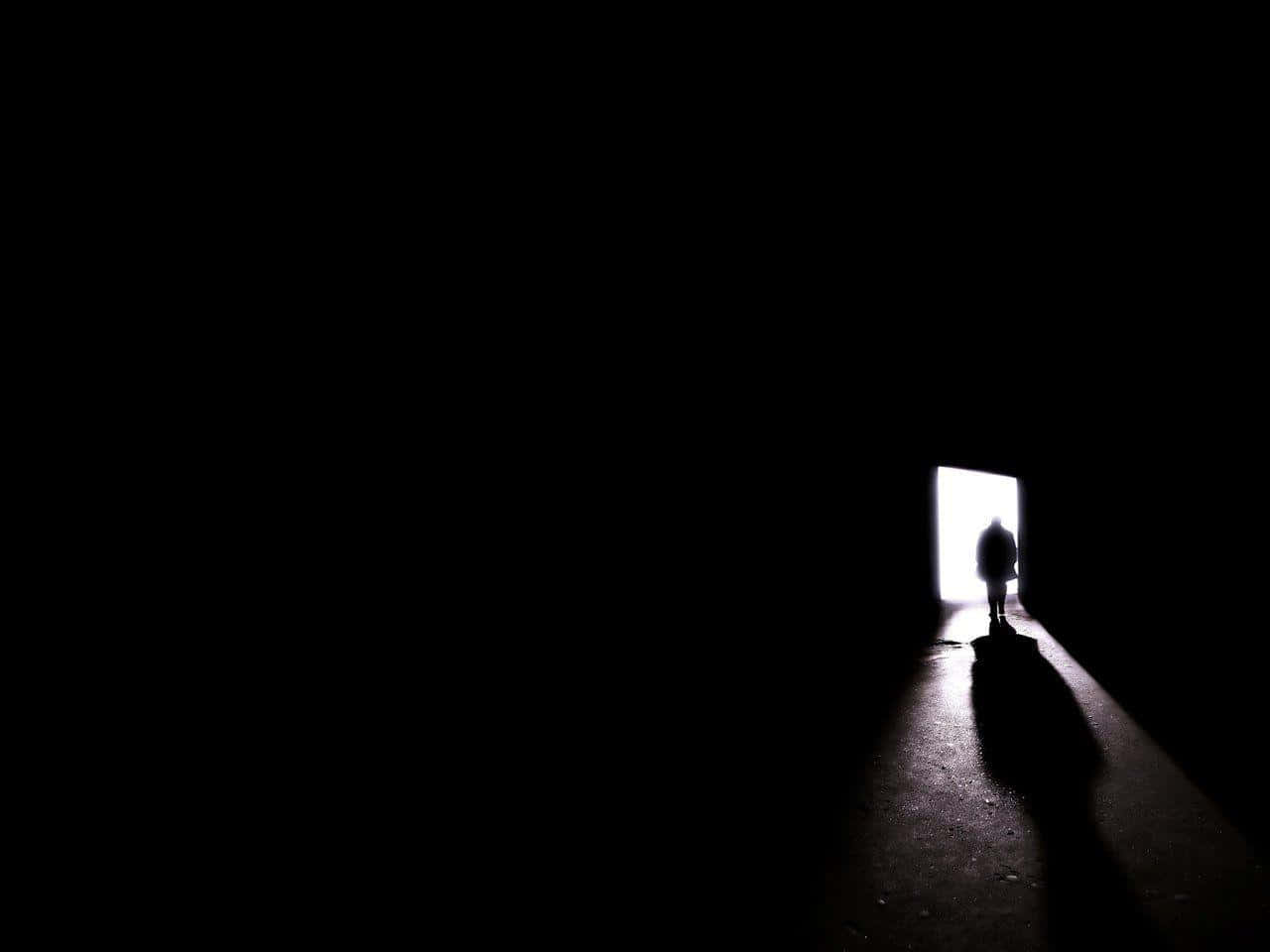 shadow 桌布 壁紙 — 一個孤獨的剪影站在明亮的門口門檻上，在漆黑一片的隧道中投下長長的影子。